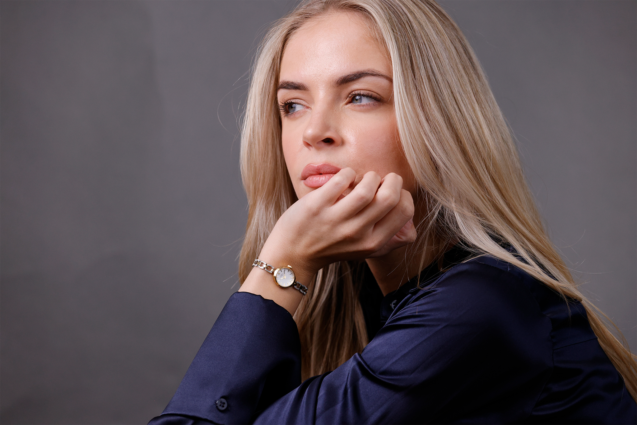 Woman with blonde hair wearing a Rotary 1895 watch and a dark blue shirt against a gray background