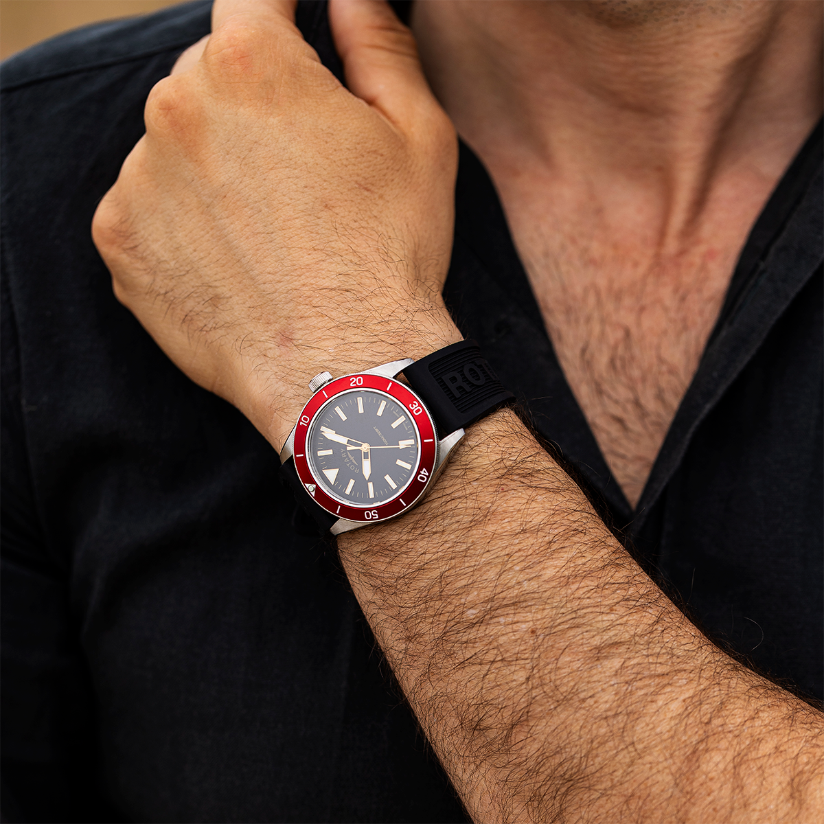 Close-up of a wrist wearing a Rotary Apex100 watch with a dark face and red bezel