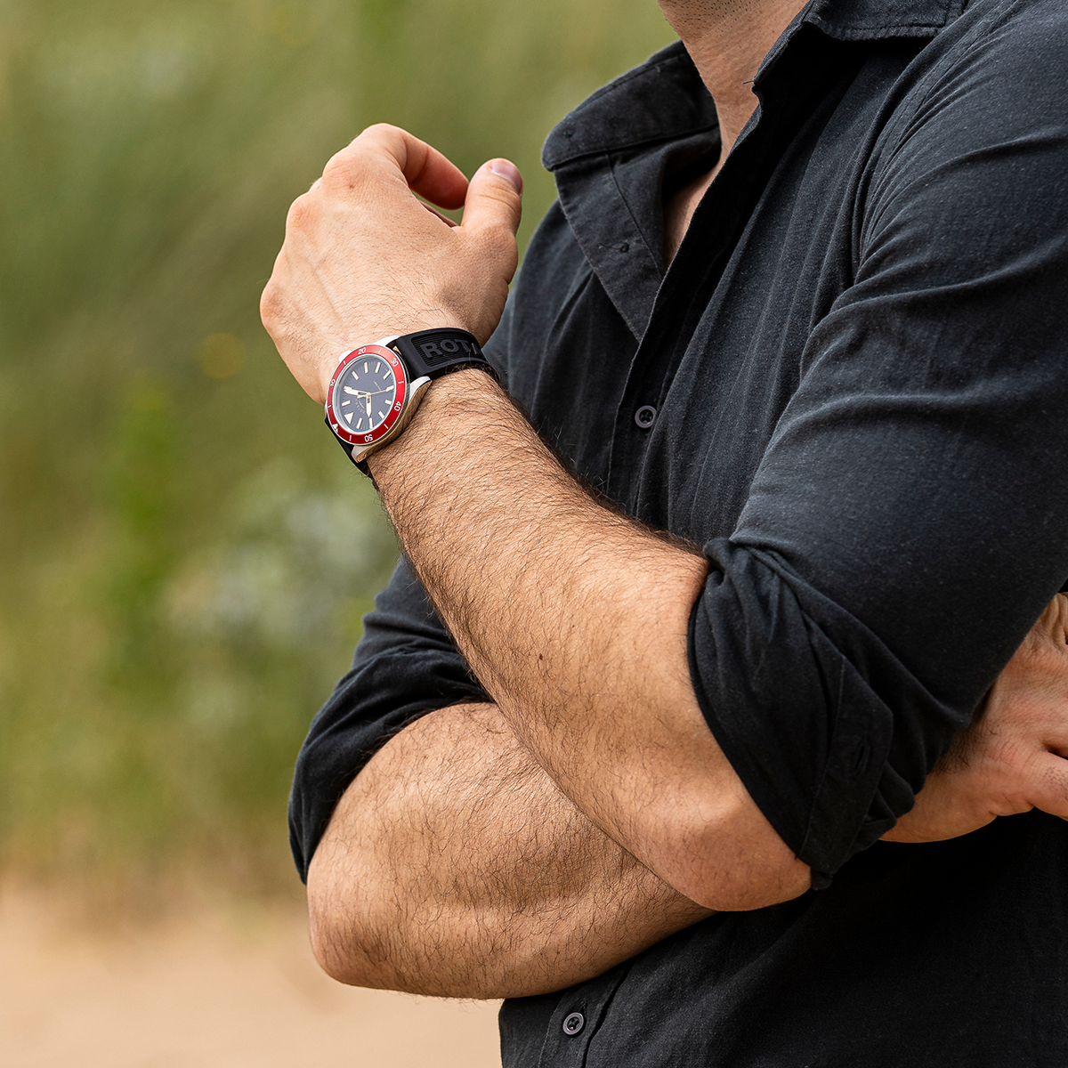 Person wearing a black shirt and a Rotary Apex100 watch with a blurred natural background