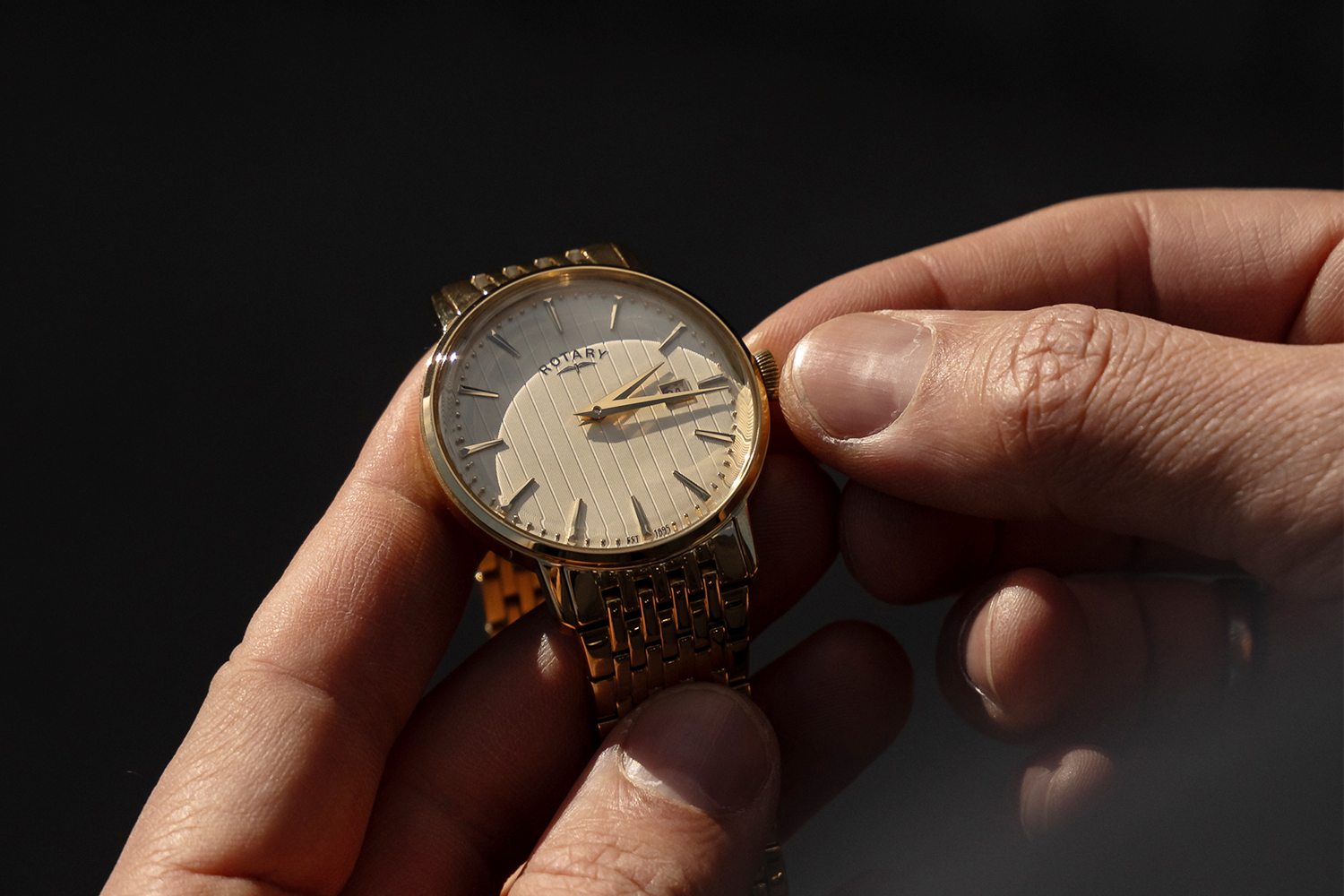 Gold Rotary wristwatch held in a hand against a dark background