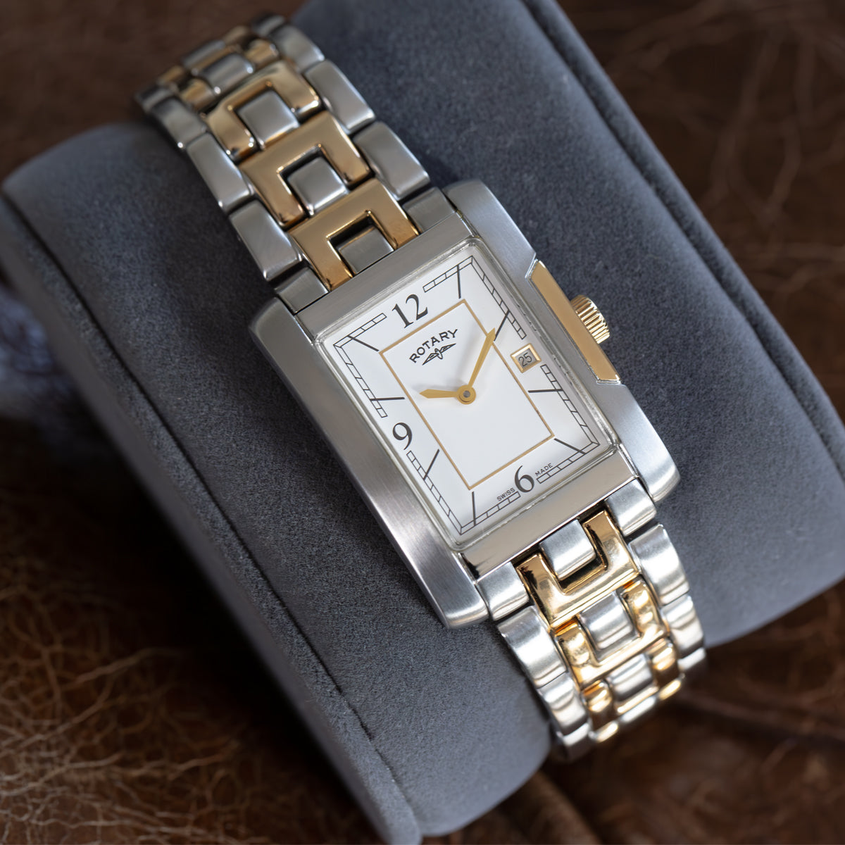 A Rotary Savannah Swiss Made watch with a white dial, featuring gold hands and hour markers, a two-tone bracelet with alternating stainless steel and gold-tone links, displayed on a grey cushion.