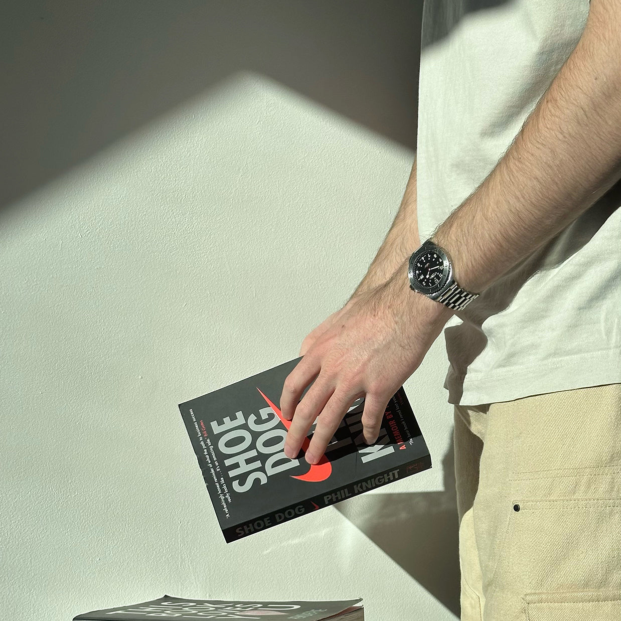 A man wearing a mens rotary watch in stainless steel with a black dial. he is also holding a book in his hands