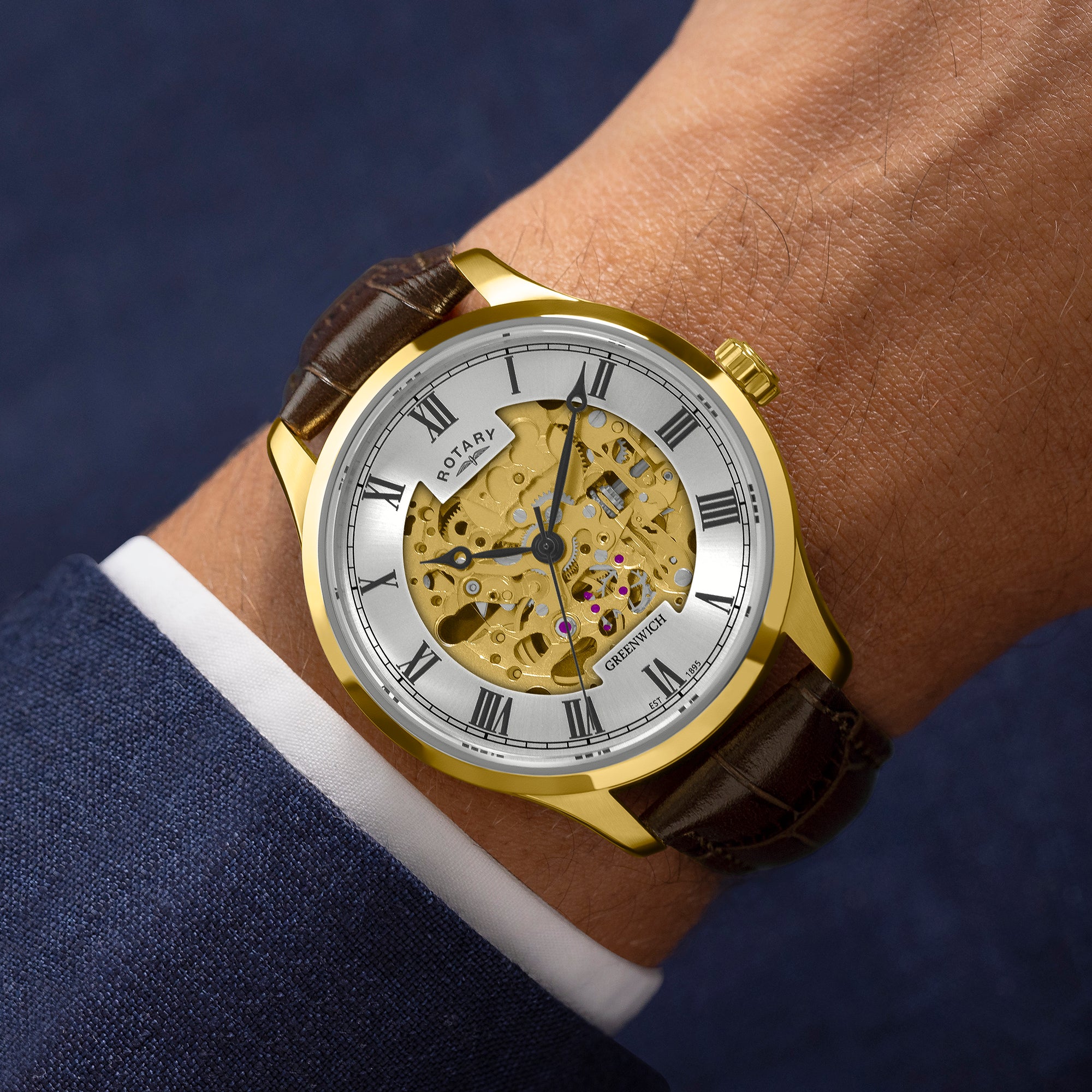Gold wristwatch with brown leather strap on a wrist, against a dark background