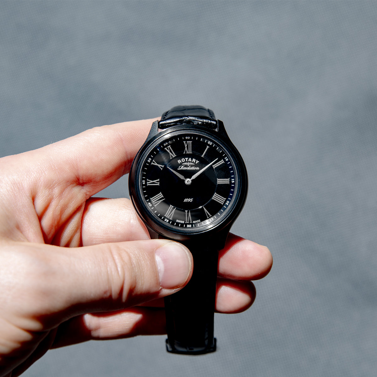 Hand holding a black Rotary wristwatch with a gray background