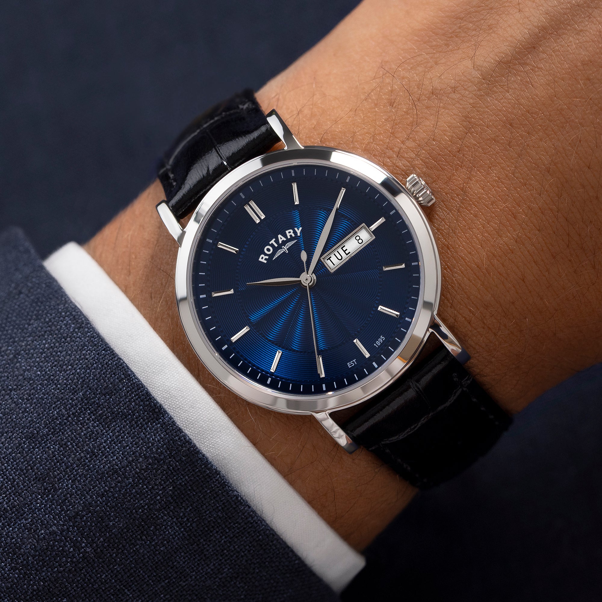 Rotary watch with blue dial and black strap on a wrist against a dark background