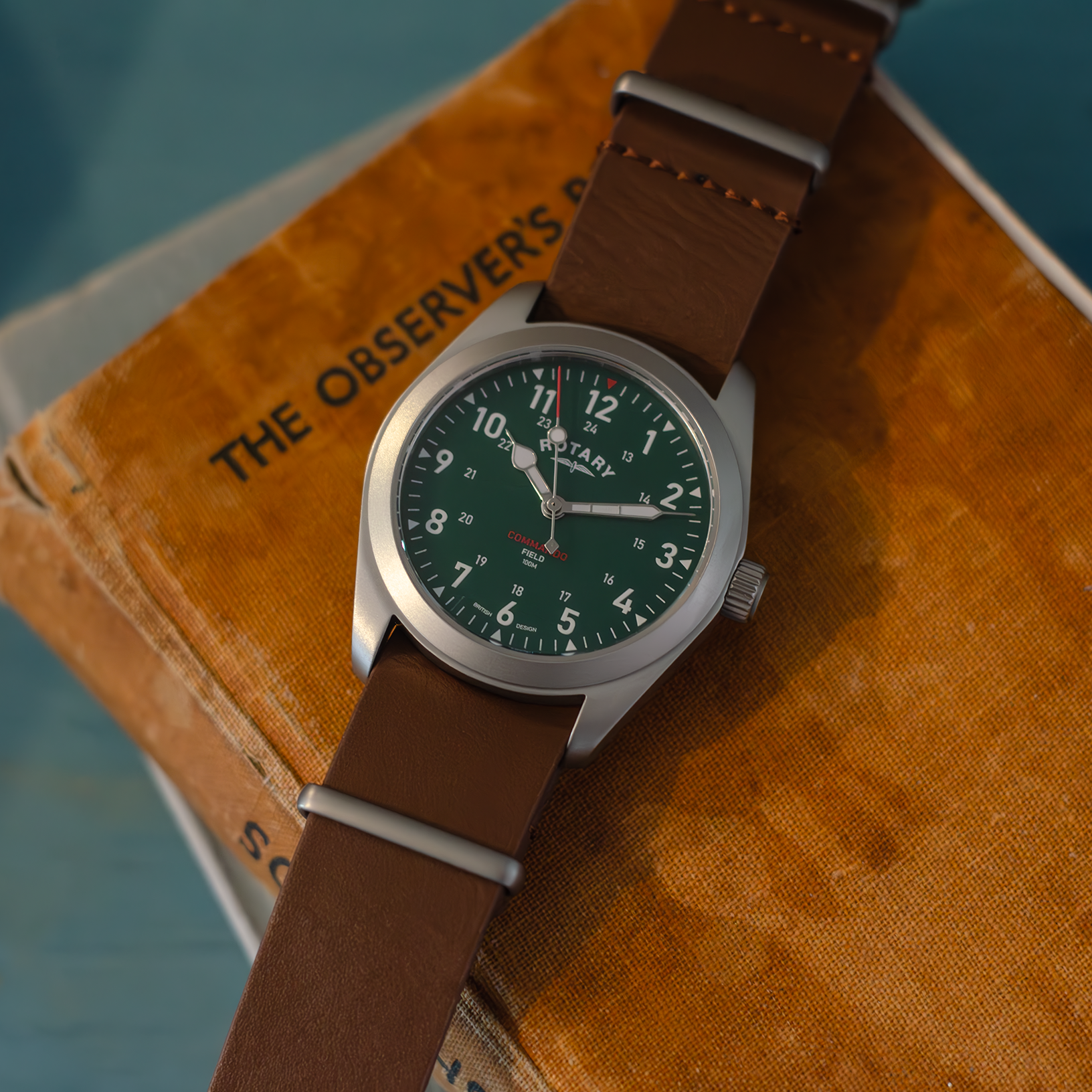 Rotary military style watch in stainless steel with a green dial and brown leather nato strap. Pictured against a set of vintage books