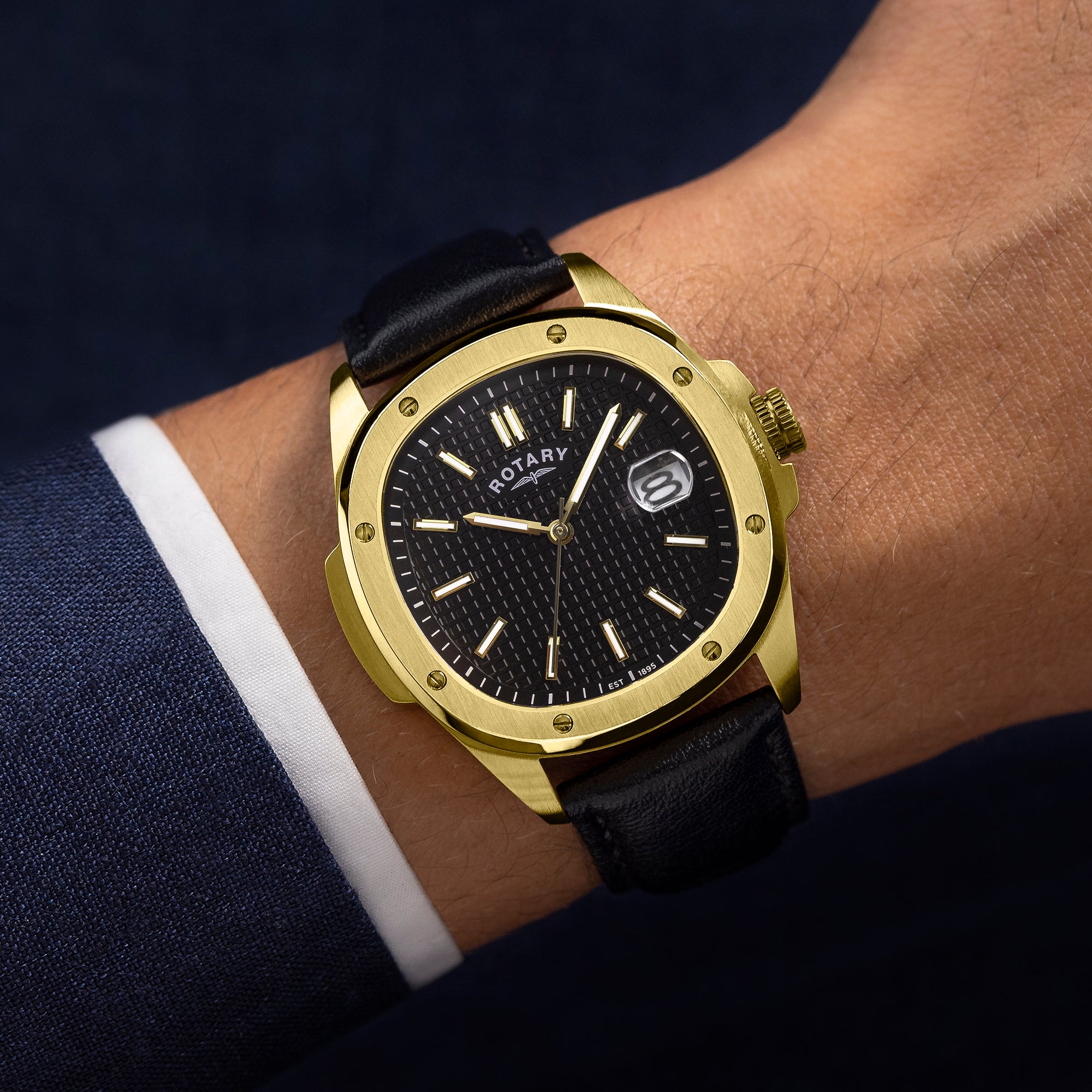 Gold Rotary wristwatch with black leather strap on a person's wrist against a dark background
