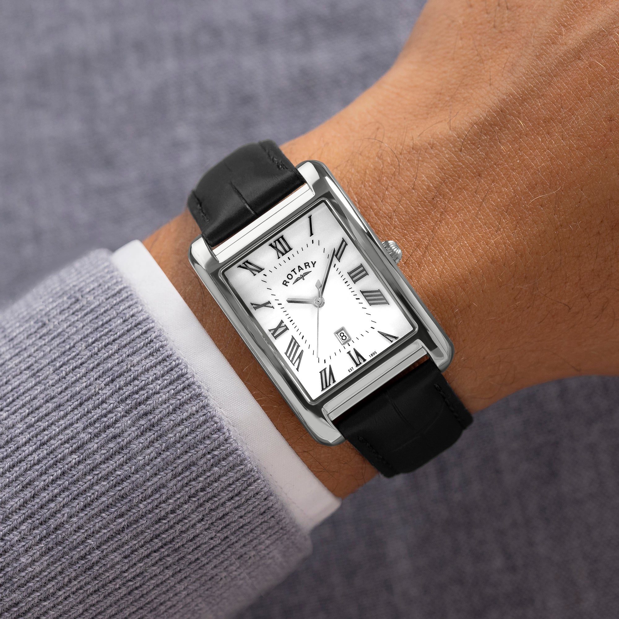 Rectangular Rotary watch with black strap on a wrist against a gray background