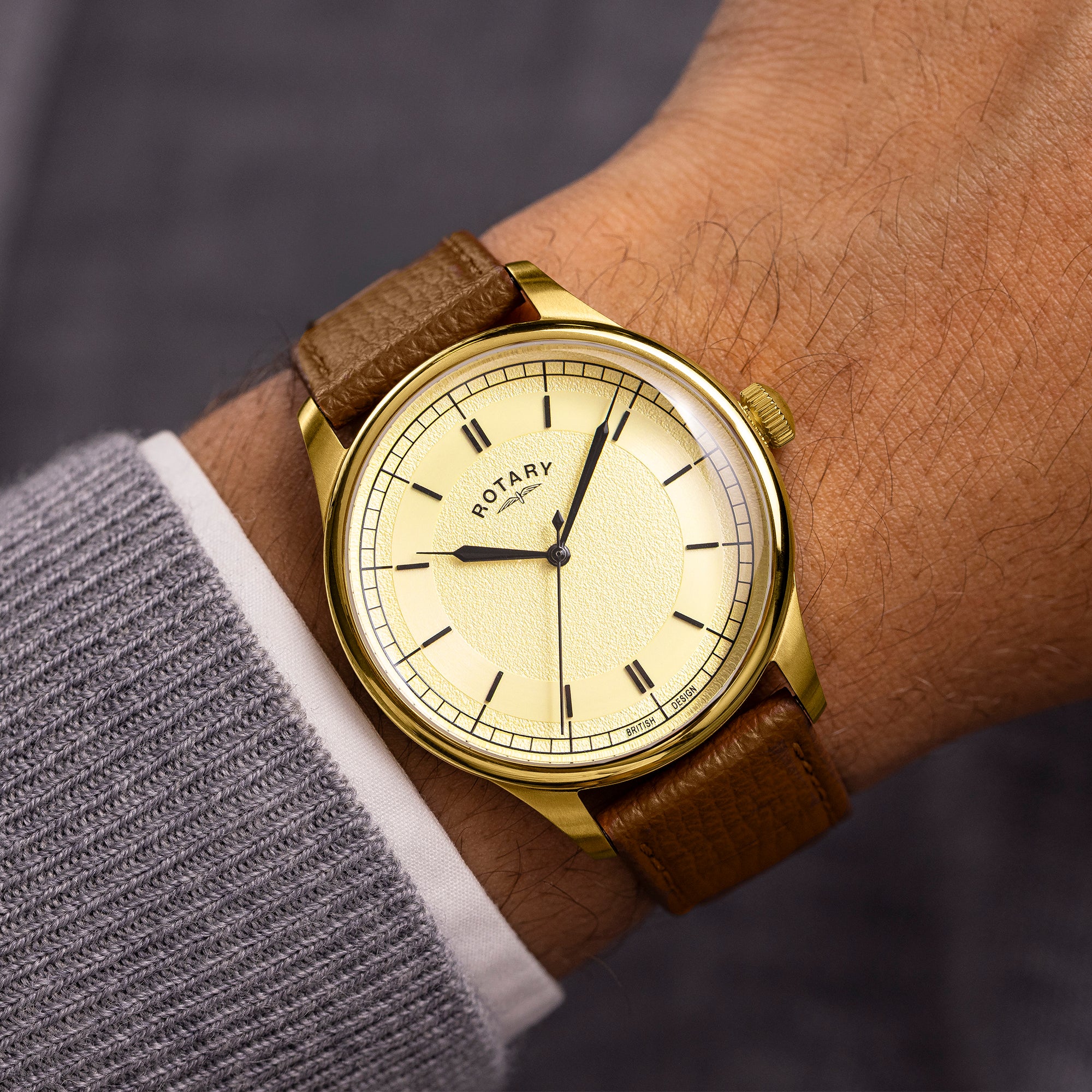 Gold wristwatch with brown leather strap on a person's wrist against a blurred background