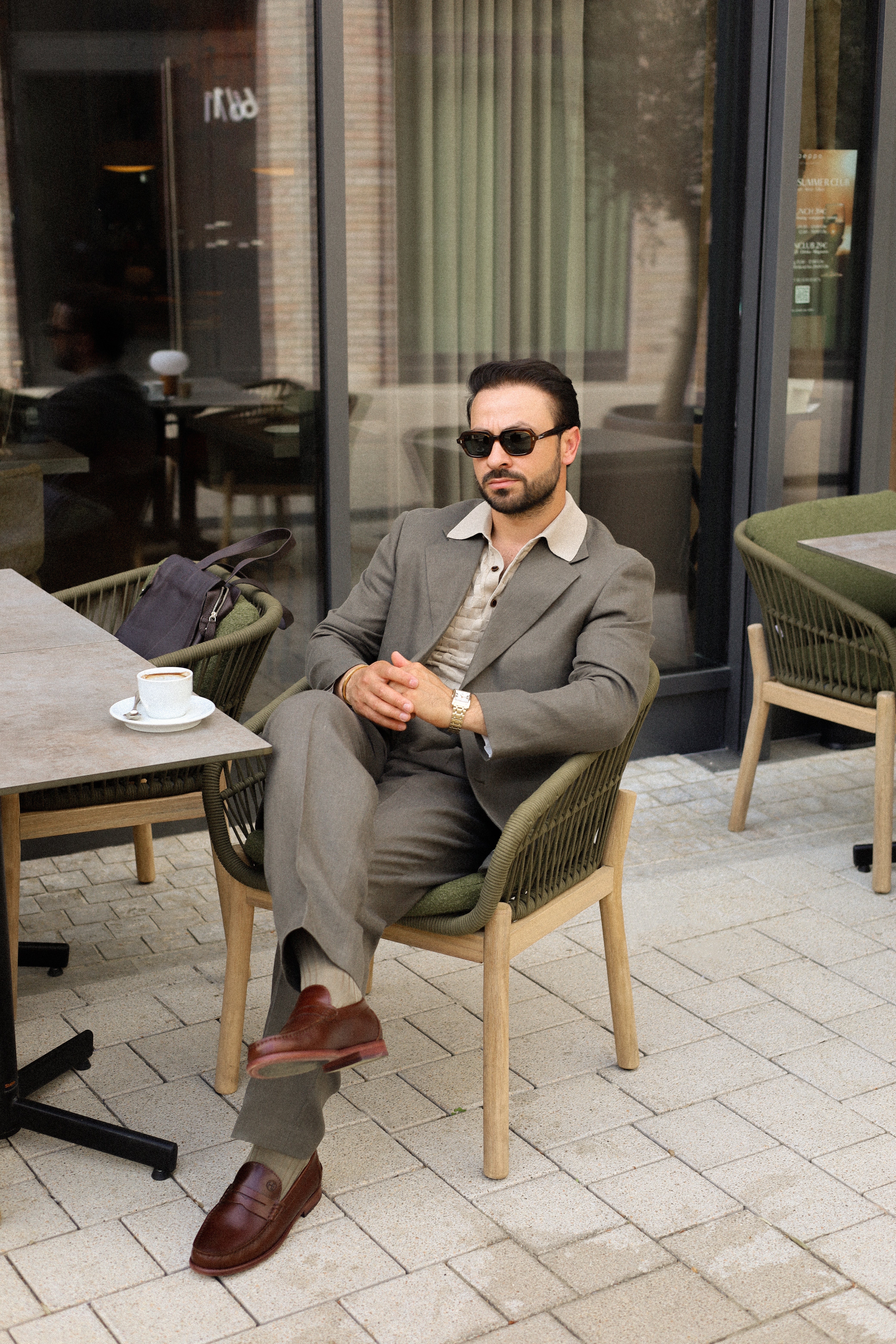 Man in a suit sitting at an outdoor cafe table with sunglasses on wearing a gold Rotary watch.