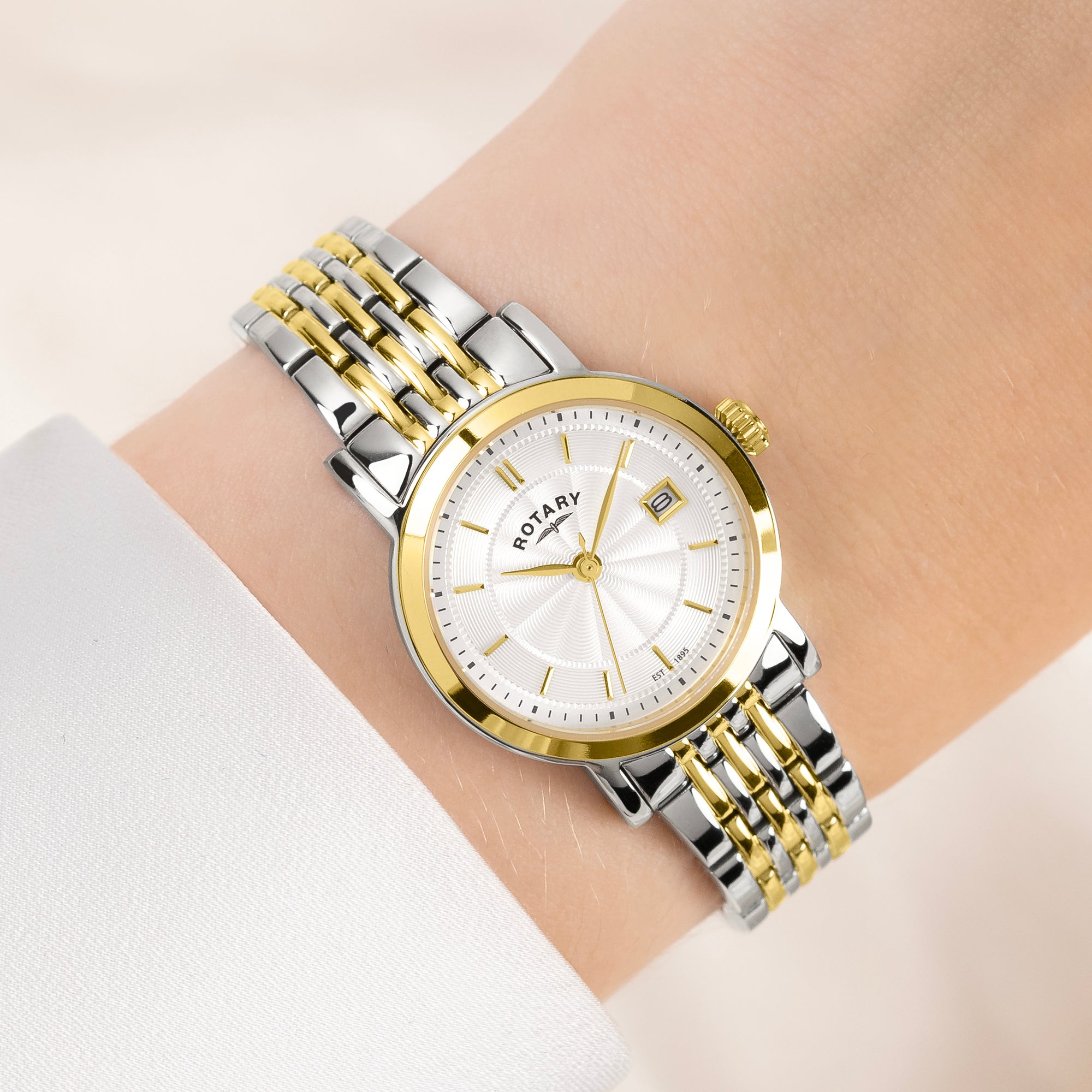 Two-tone Rotary silver and gold watch on a wrist with a light background