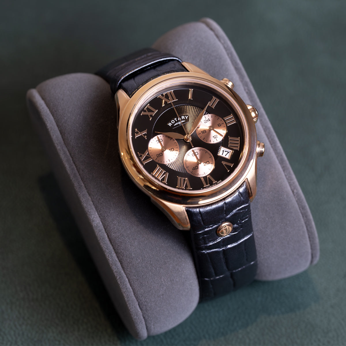Rotary watch with black leather strap and gold accents on a gray cushion