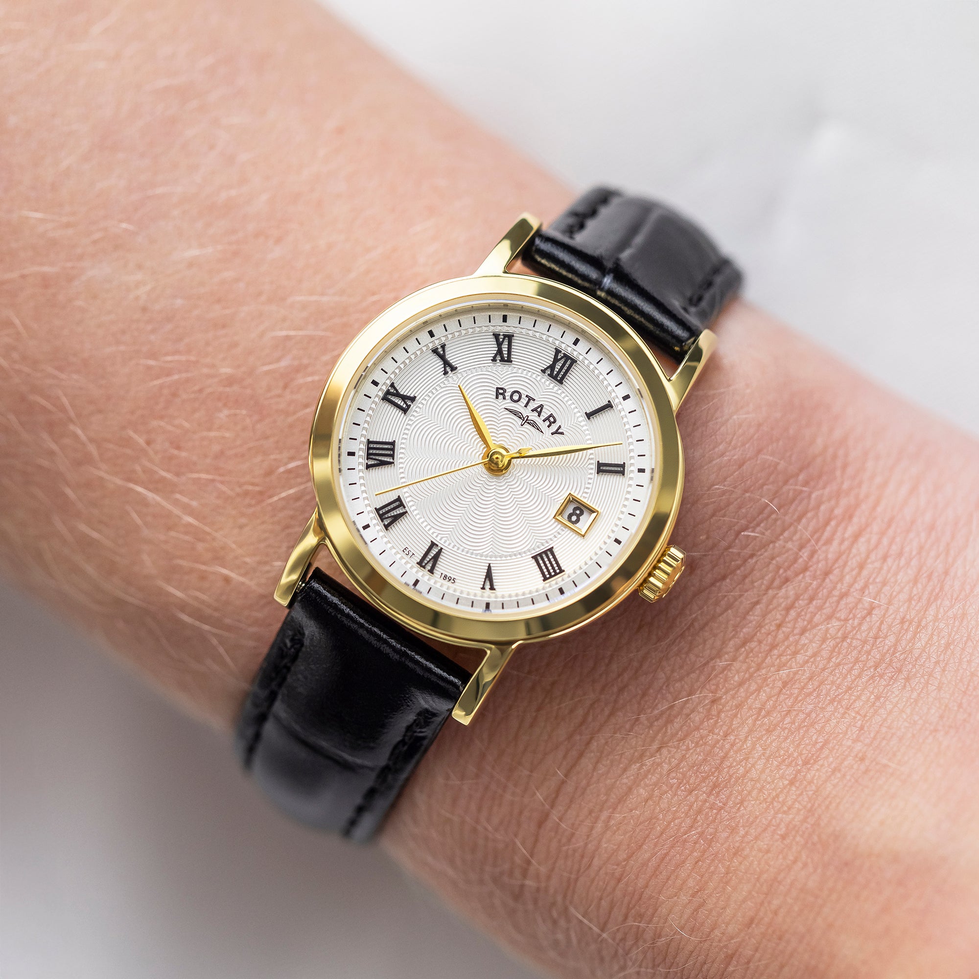 Gold wristwatch with black leather strap on a wrist against a neutral background