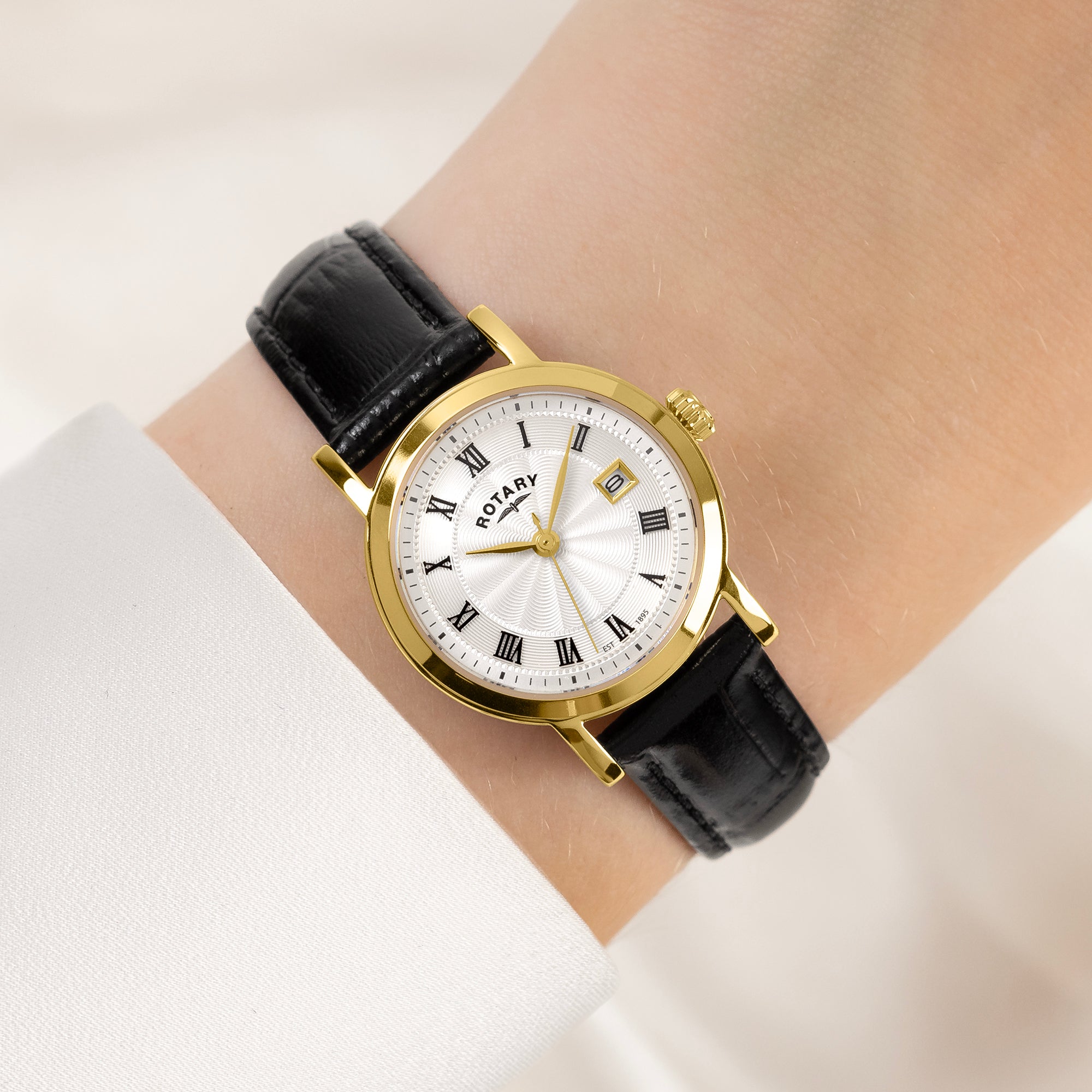 Gold Rotary wristwatch with black leather strap on a wrist against a light background