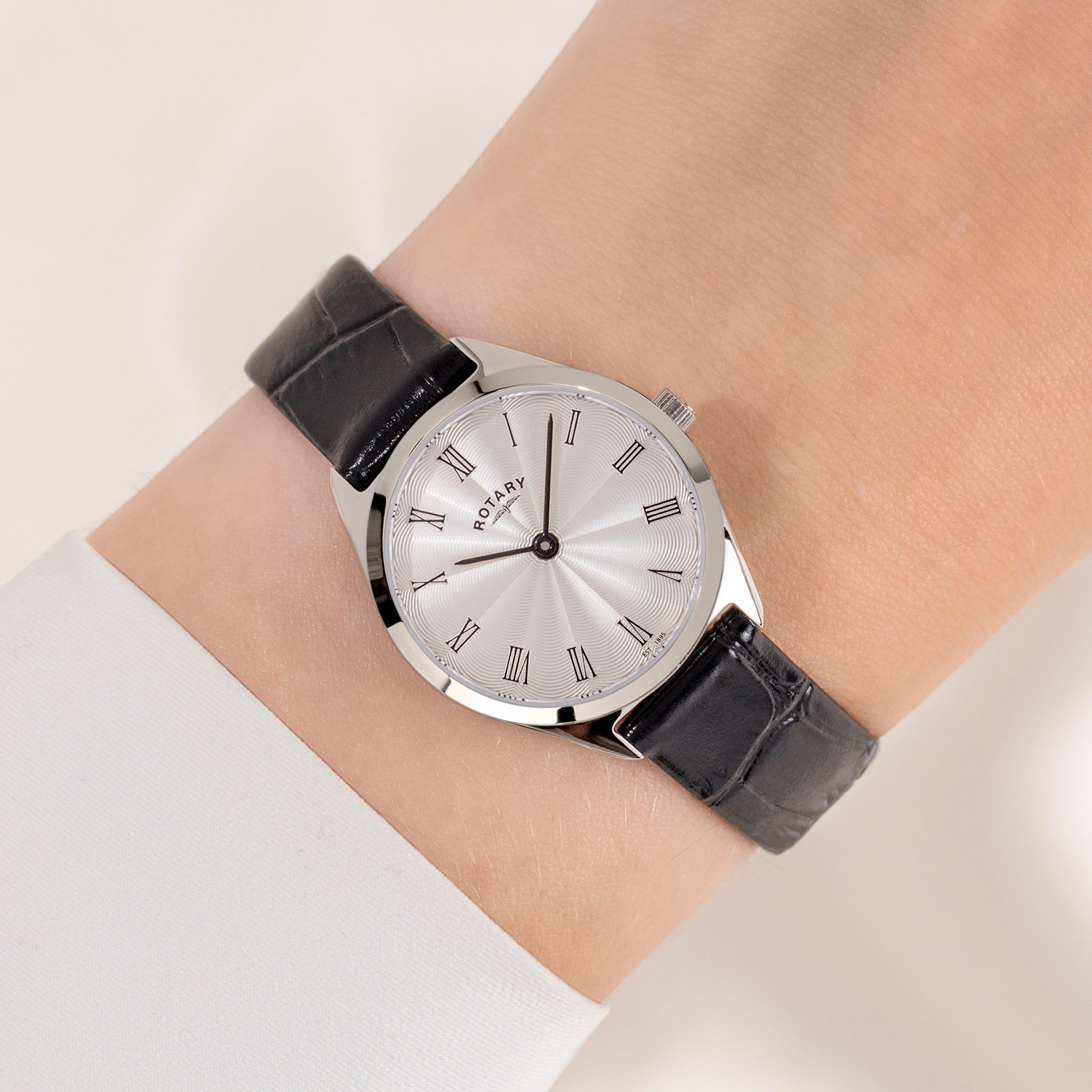 Wrist wearing a Rotary watch with a silver case on a light background