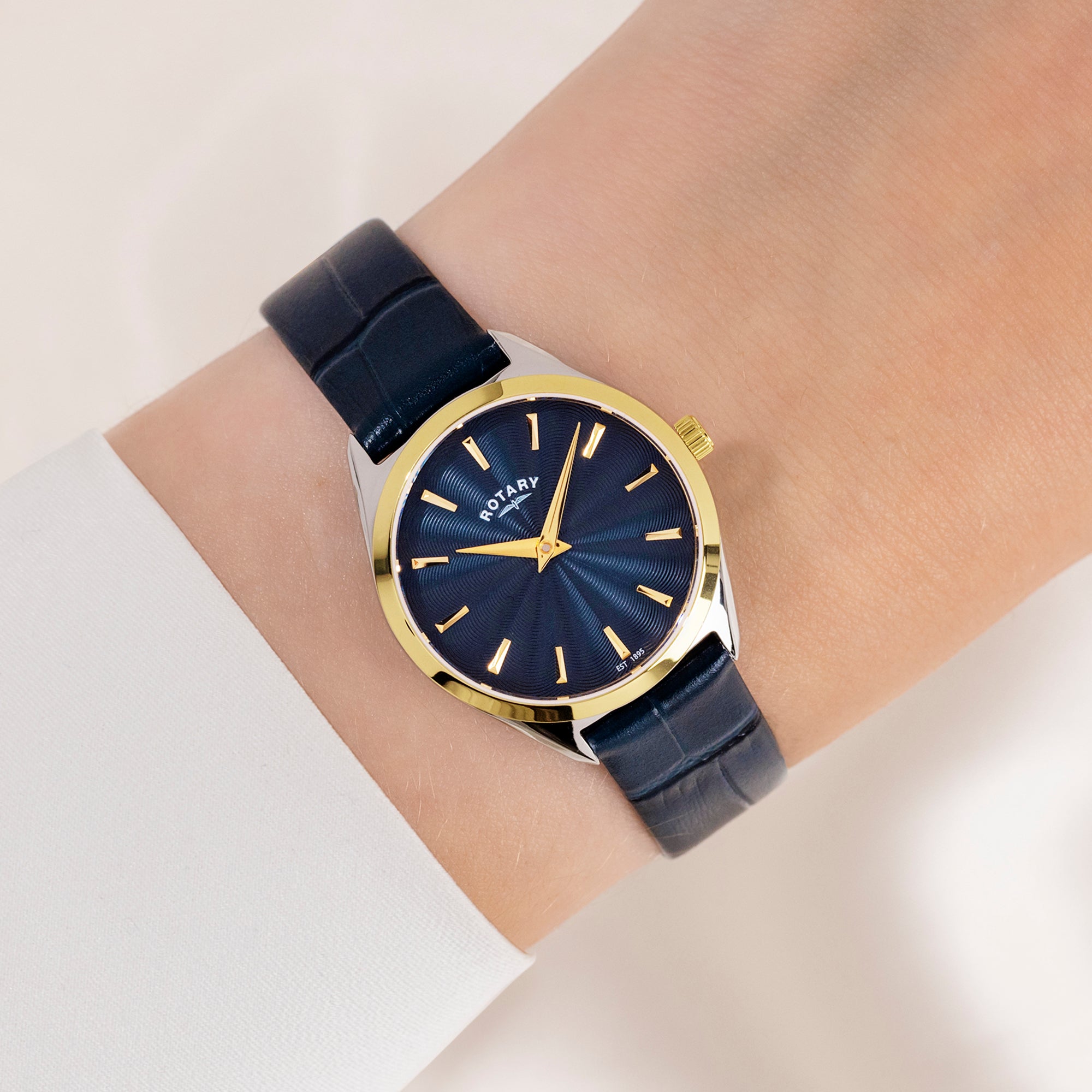 Wrist wearing a blue Ultra Slim Rotary watch with a blue face on a light background