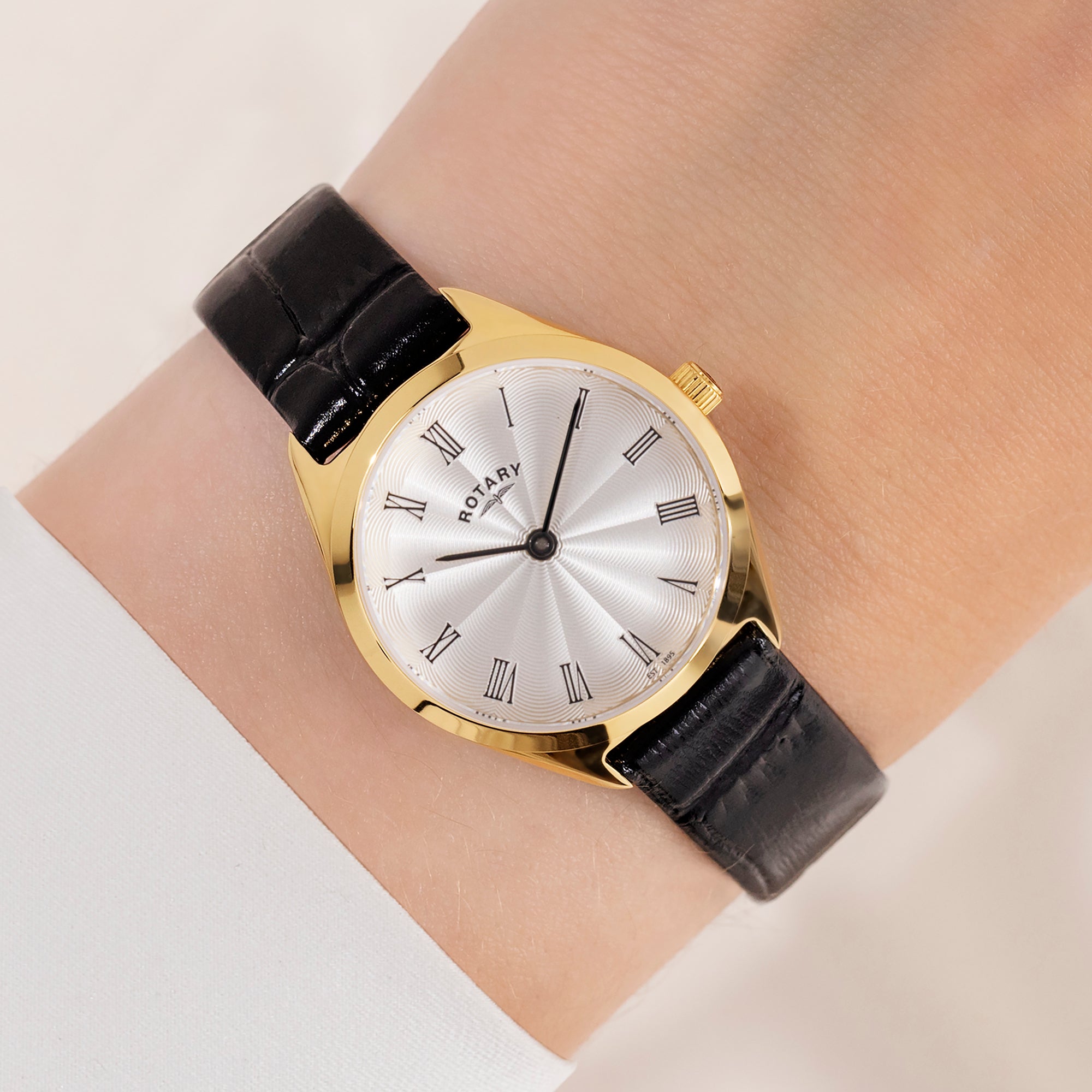 Gold Rotary watch with black leather strap on a wrist against a neutral background