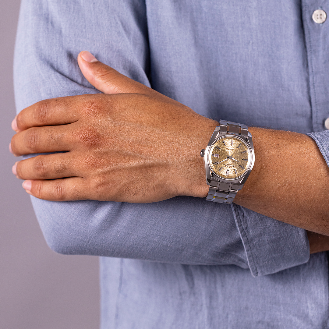 Hand wearing a gold dial Lumen with a silver case and bracelet on a blurred background