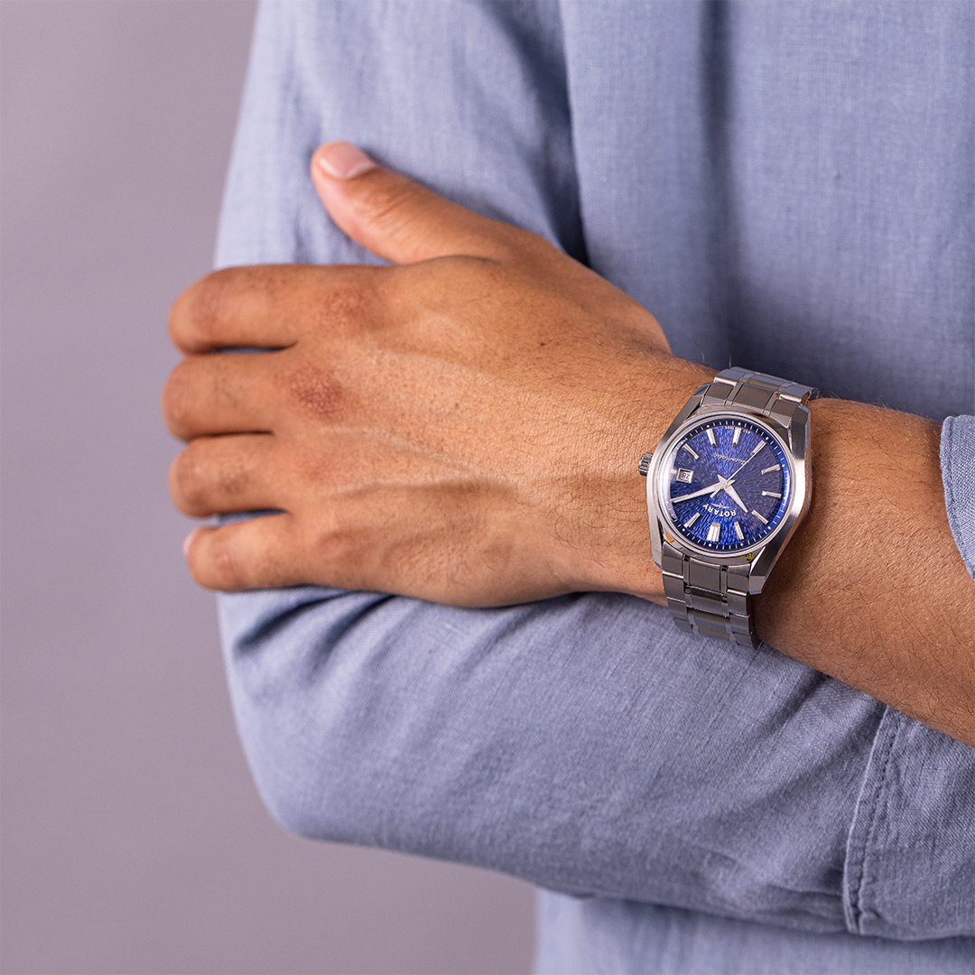 Person wearing a silver watch with a blue face on a plain background