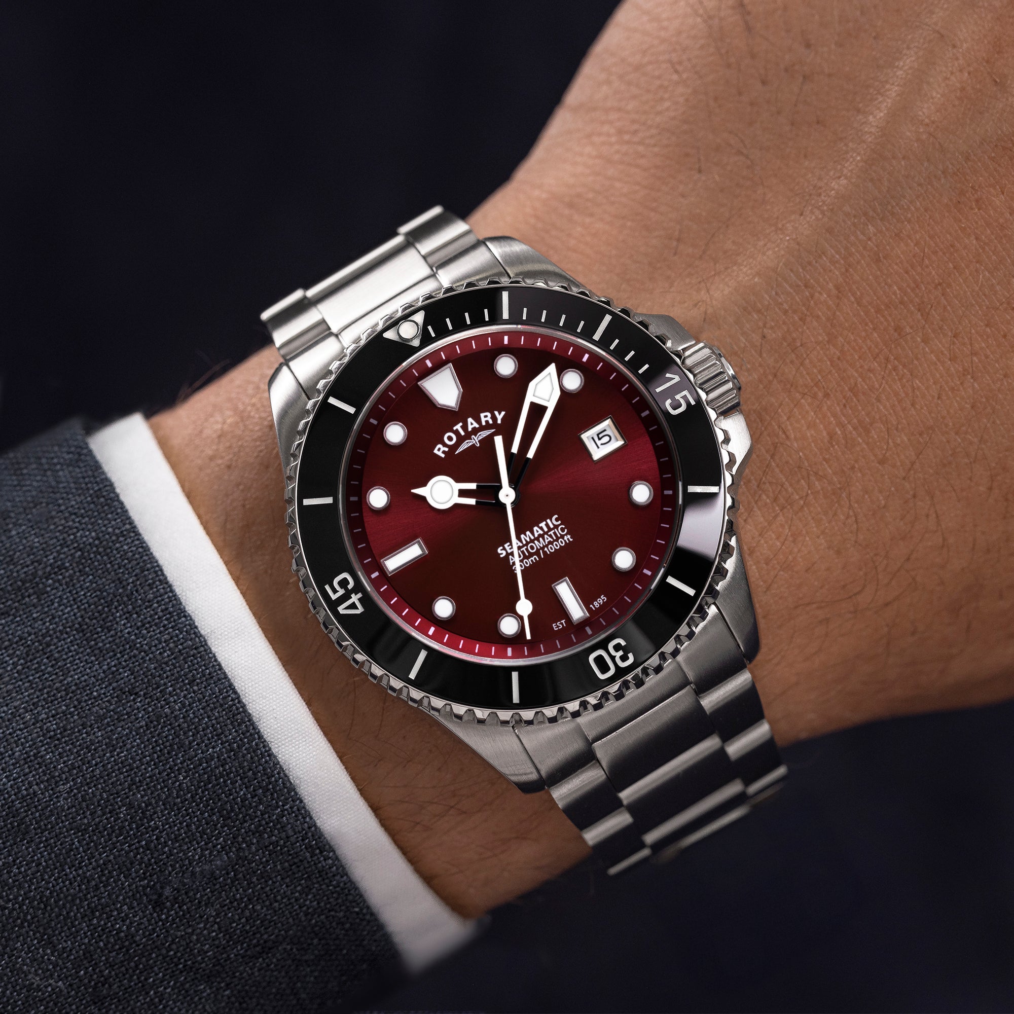 Rotary Seamatic watch with a red face and silver bracelet on a wrist against a dark background