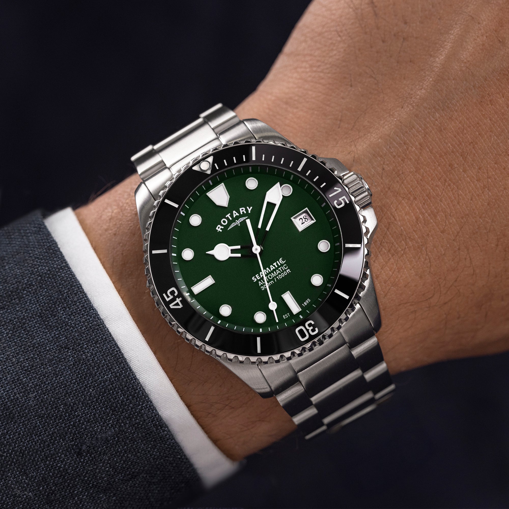 Rotary watch with green dial and silver bracelet on a wrist against a dark background