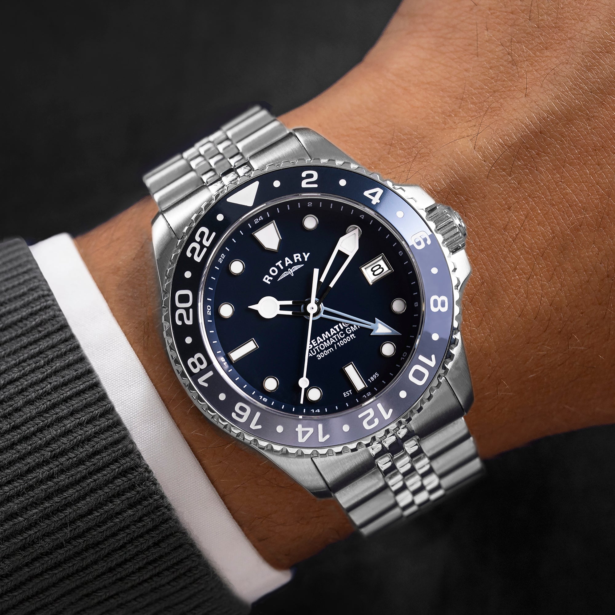Rotary watch with blue bezel and silver bracelet on a wrist.