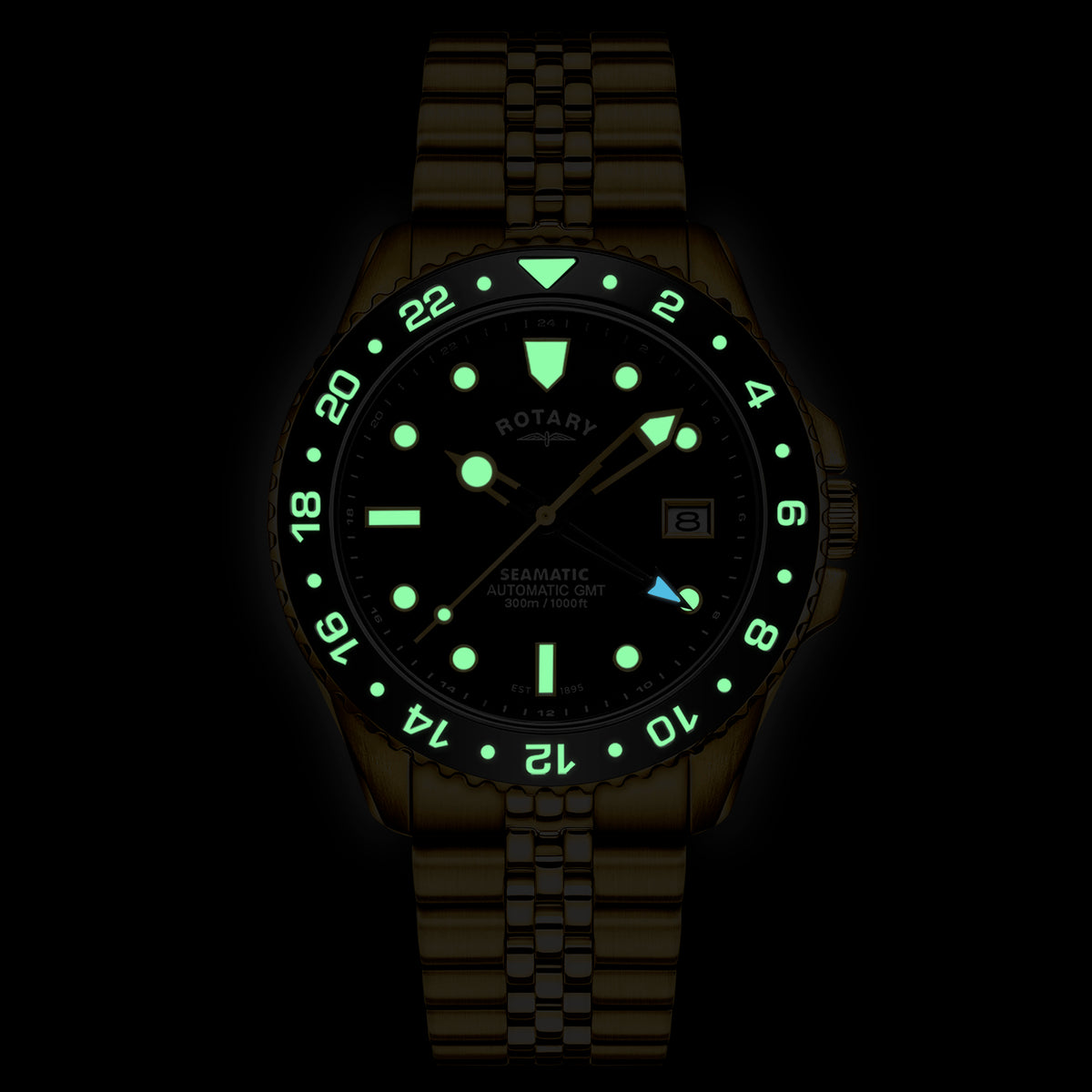 A wristwatch with a gold PVD link bracelet and a black dial, shown glowing in the dark. The dial features bright green luminous hour markers, hands, and a green bezel with white numerals.
