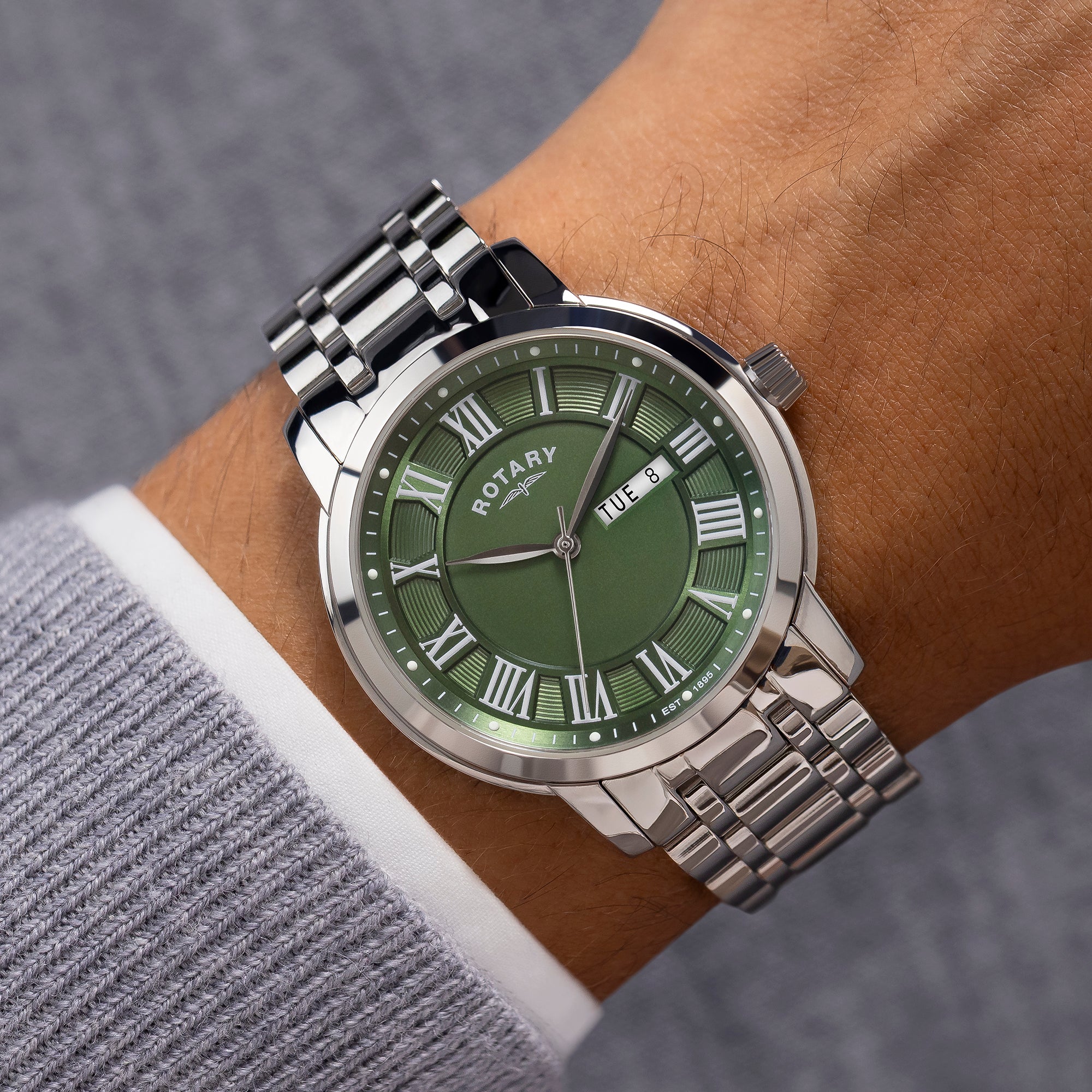 Green dial Rotary watch with silver bracelet on a wrist.