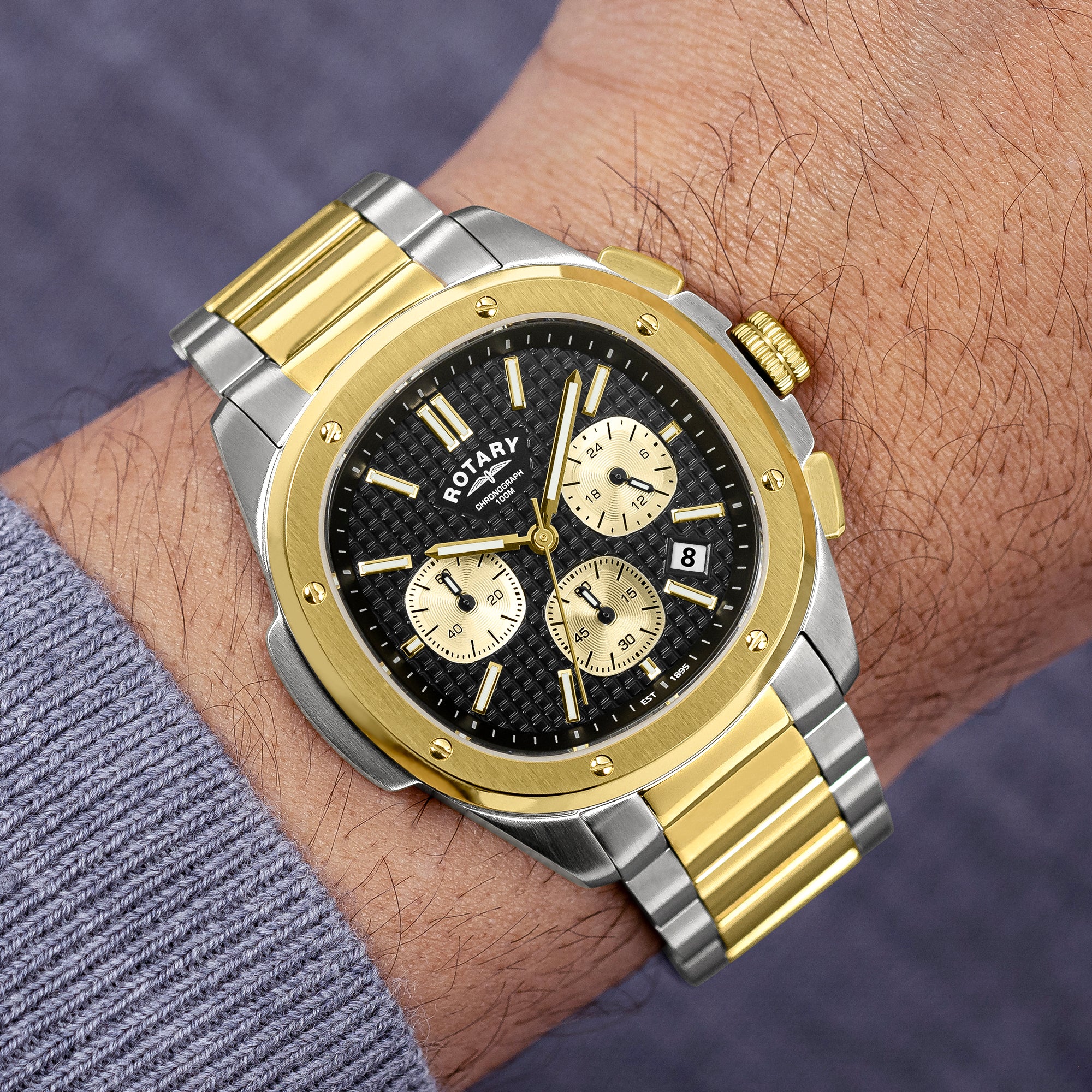 Gold and silver Rotary Apex100 Chronograph watch on a wrist with a blurred background