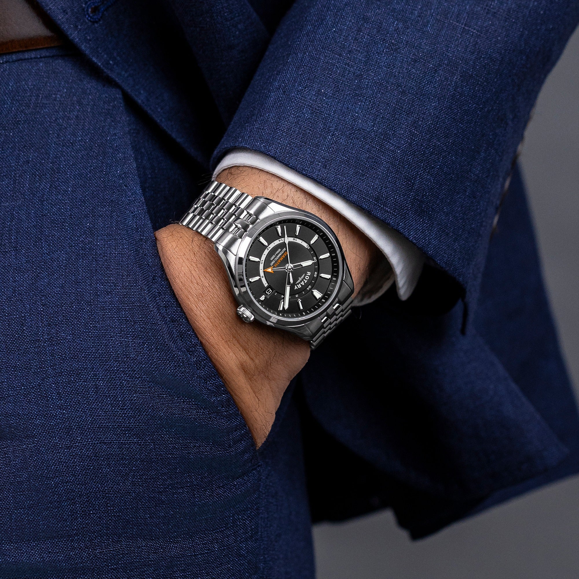 Silver Rotary Seamatic 100 GMT wristwatch on a man wearing a blue suit with a gray background