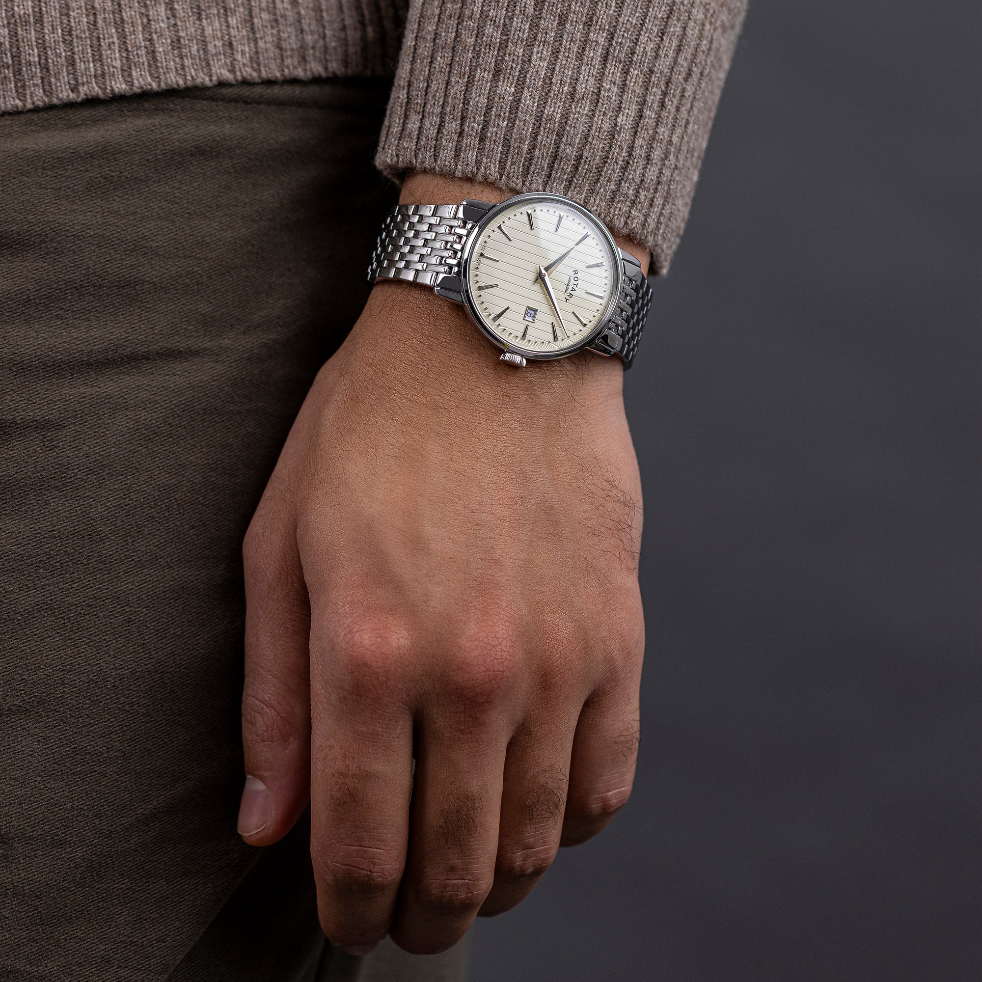 Hand wearing a silver Rotary 1895 watch with a dark background