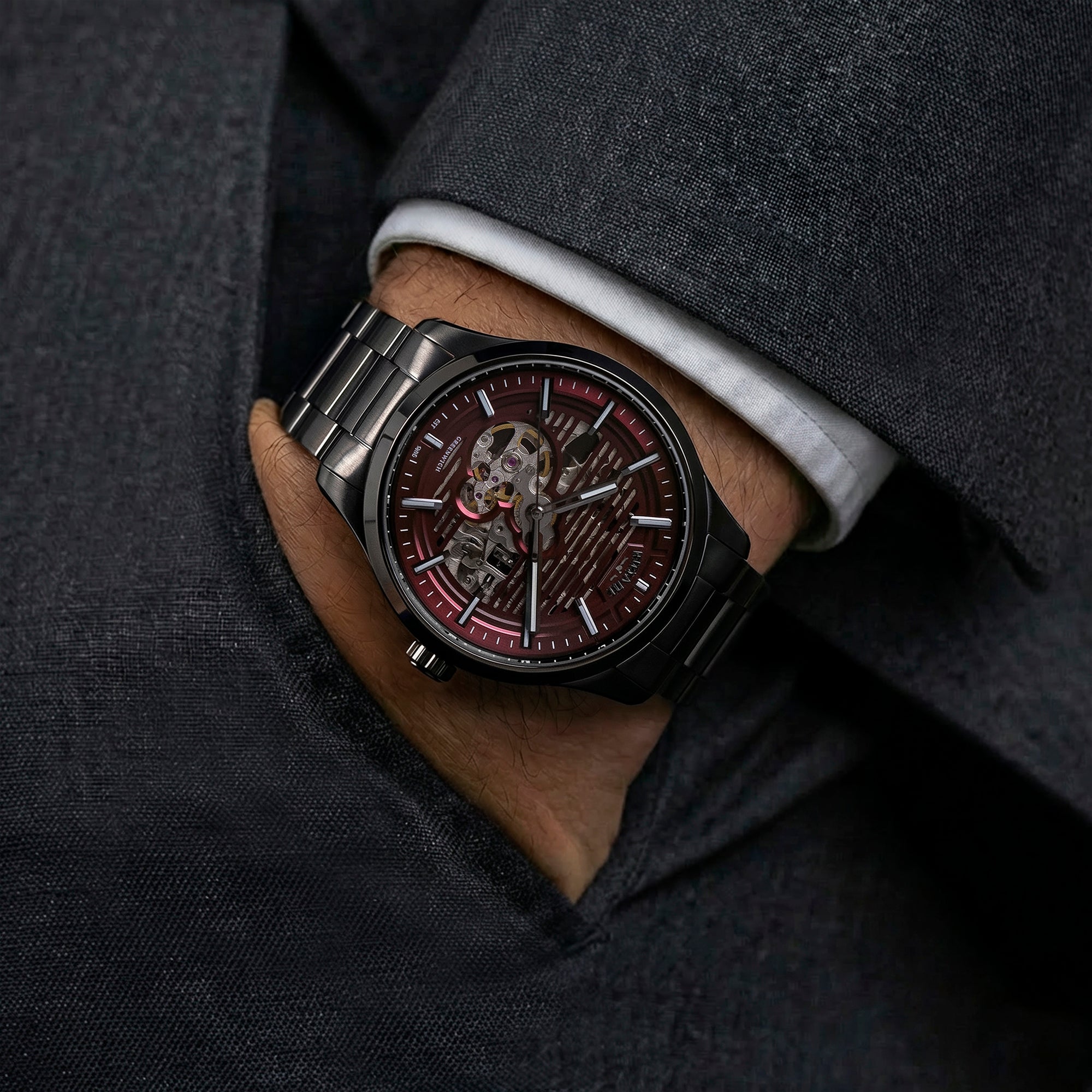 Close-up of a man wearing a dark Rotary Greenwich GT1 wristwatch with a detailed face, set against a gray suit background.