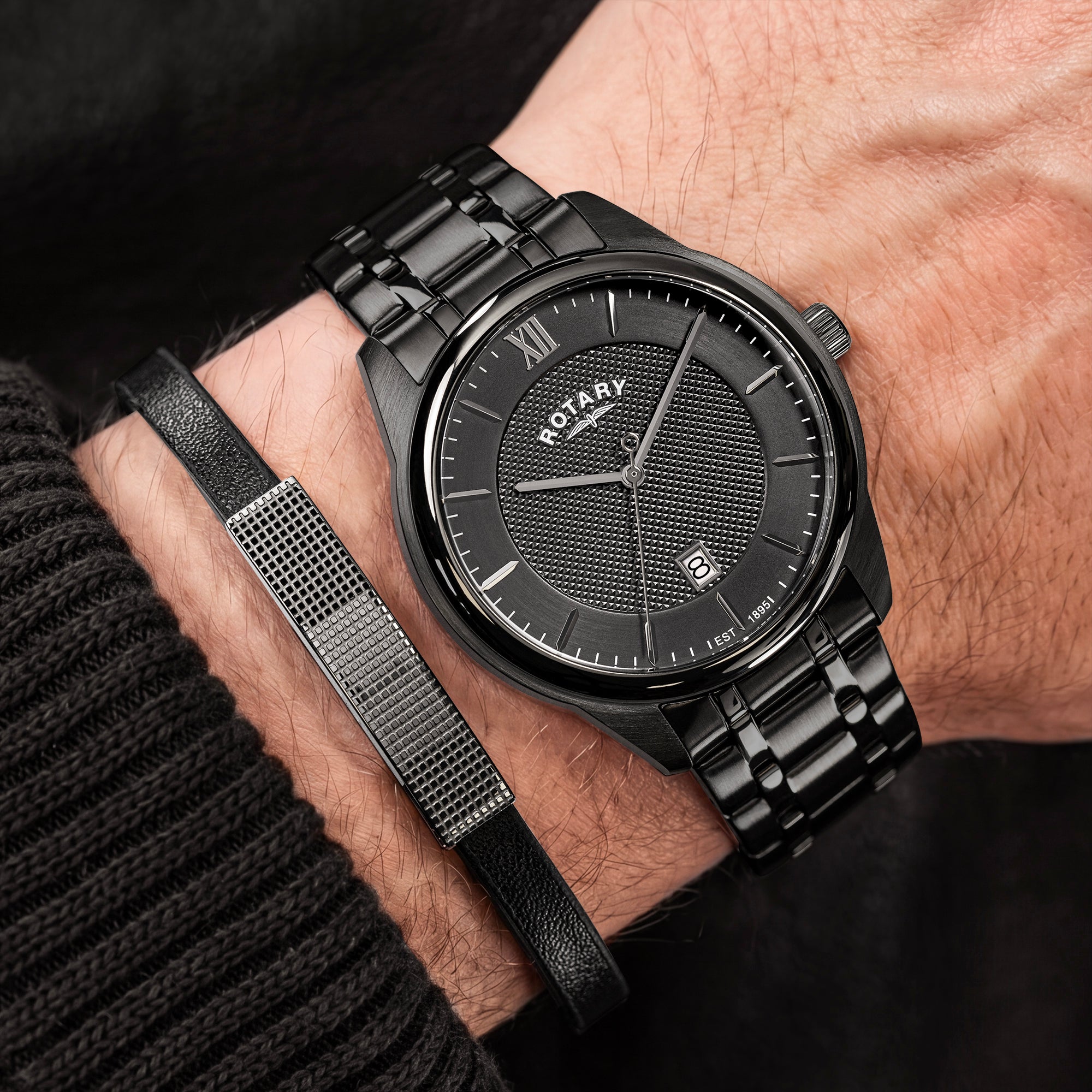 A close-up of a man's wrist wearing a black stainless steel Rotary watch, paired with a matching black leather and metal bracelet.