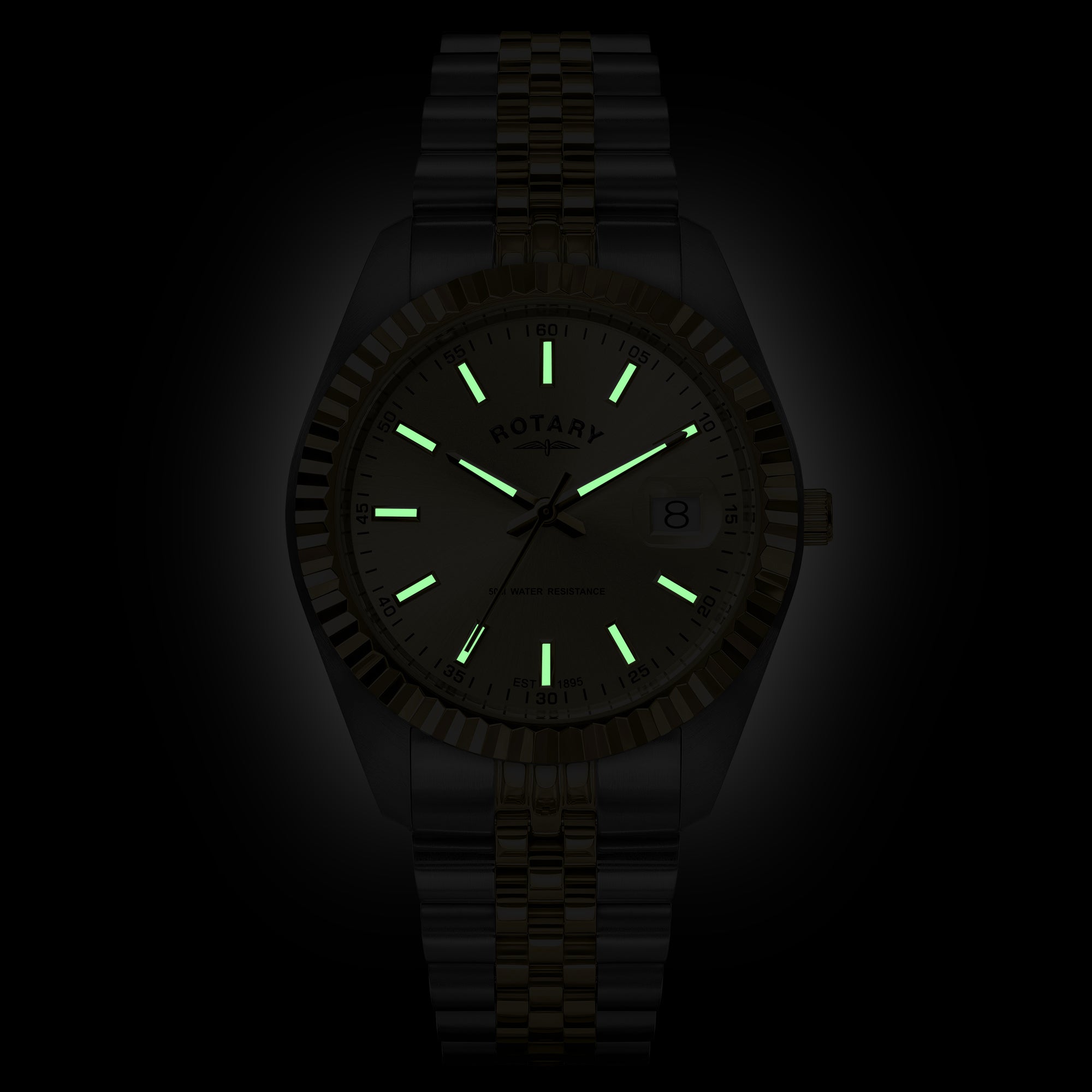 A Rotary wristwatch with a matching metal link band, shown against a black background. The watch face and bezel are very dark, but the luminous hour markers, hands, and date-day numeral glow bright green in the low light.