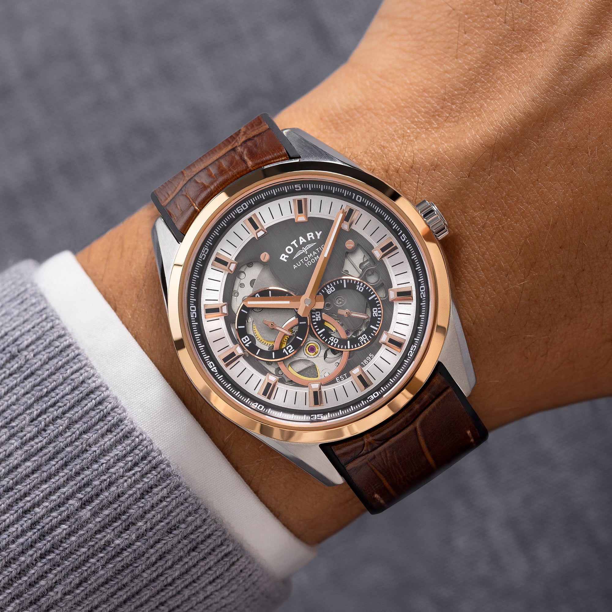 Rotary watch with brown leather strap on wrist against a neutral background