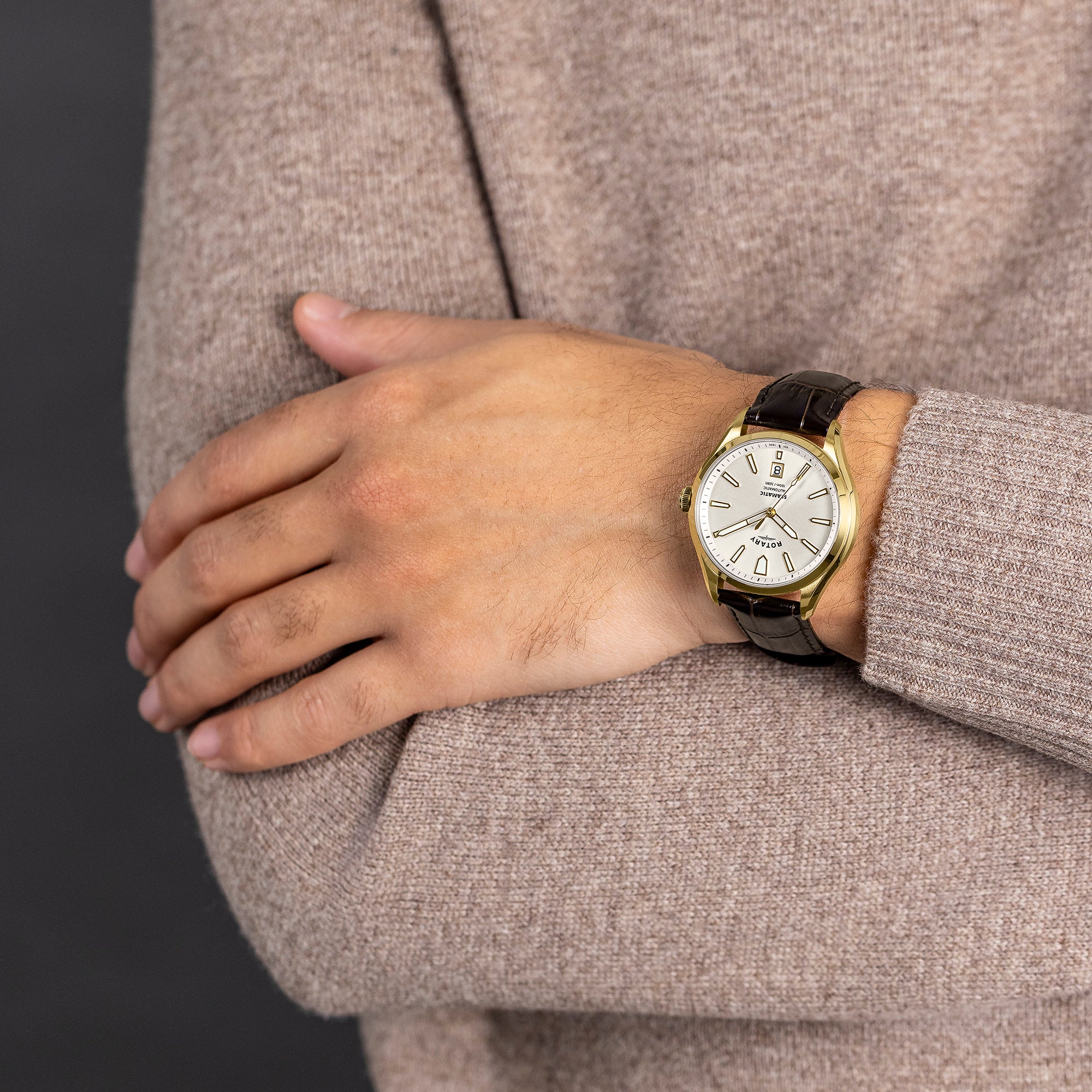 Man wearing a gold Rotary Seamatic 100 watch with a white face on a dark background