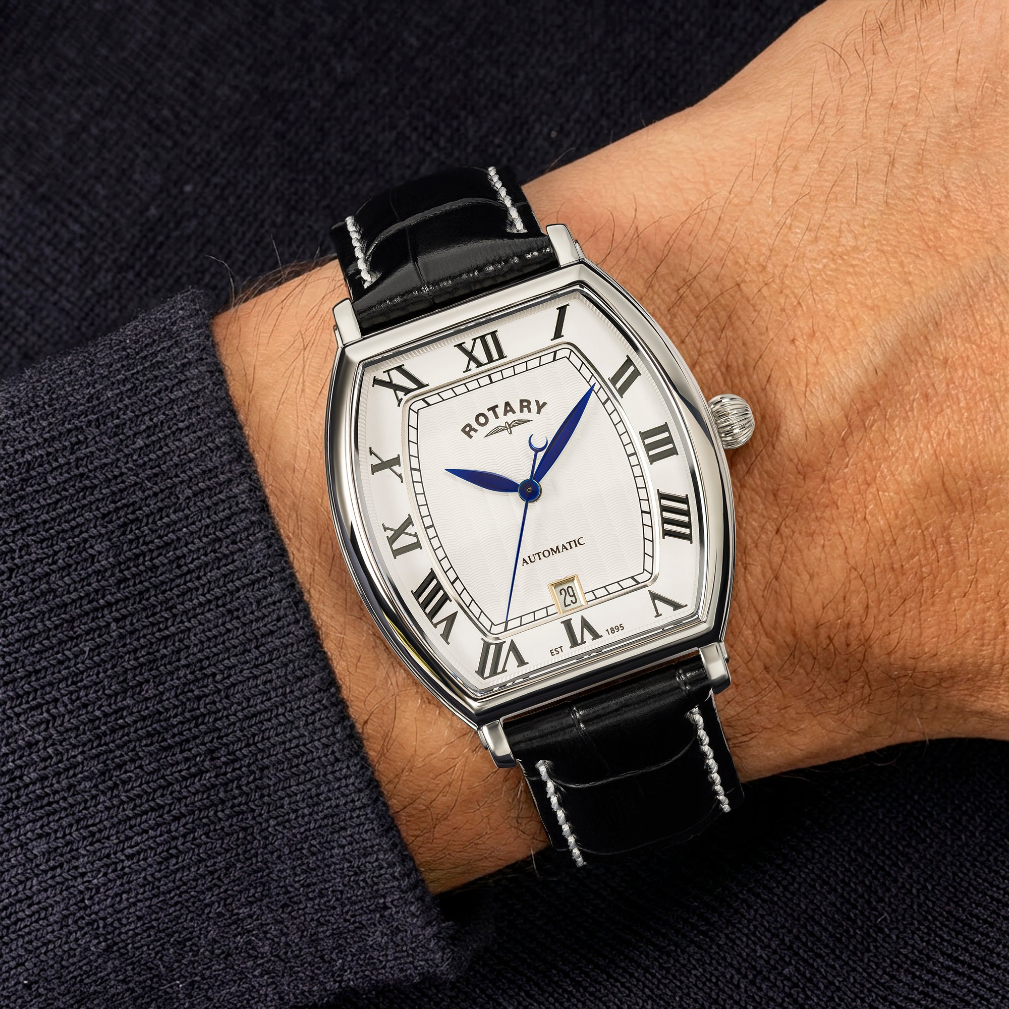 Rotary 1895 Tonneau watch on a person's wrist with a dark background