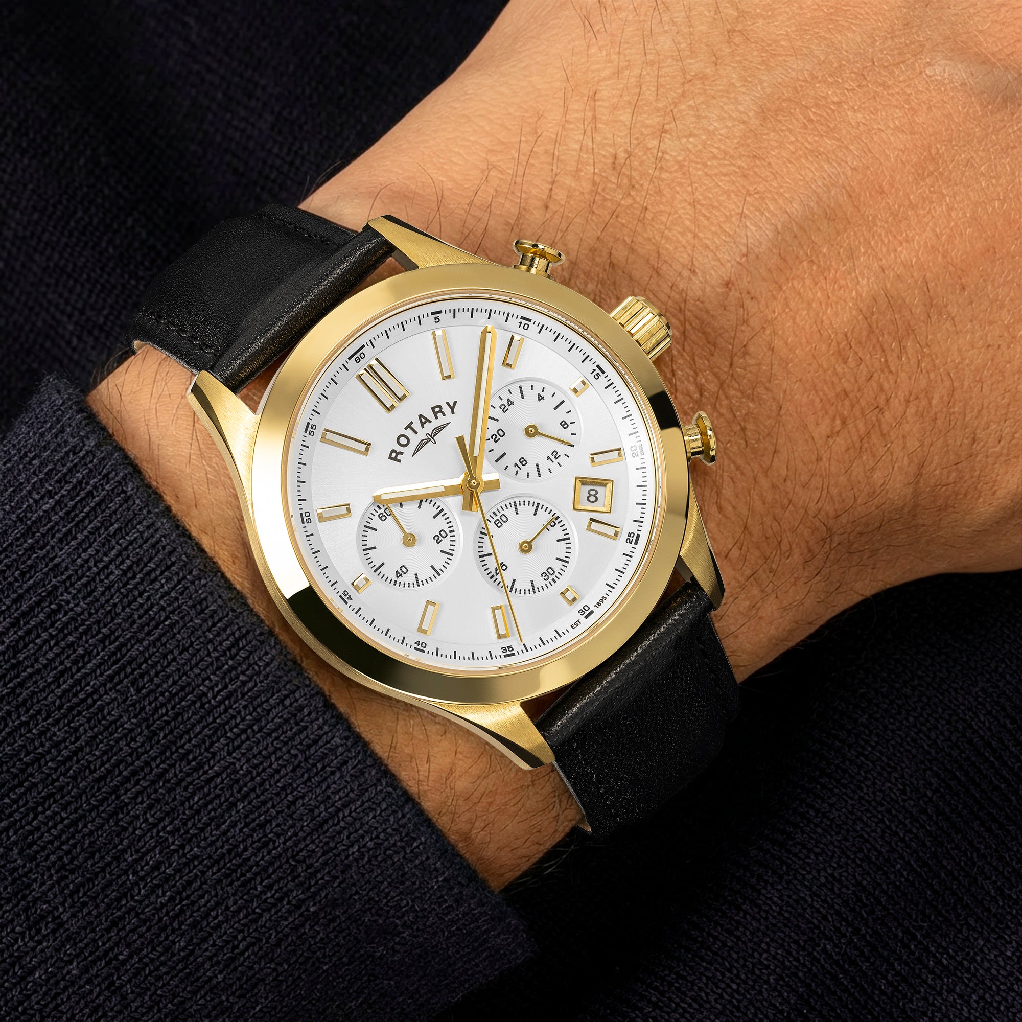 Gold Rotary Heritage Chronograph wristwatch with a black strap on a person's wrist against a dark background
