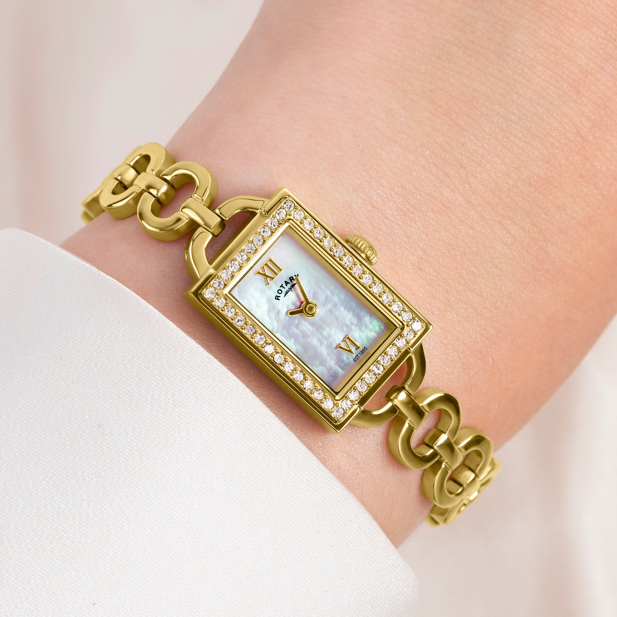 Rotary 1895 Gold wristwatch with a chain strap on a wrist against a light background
