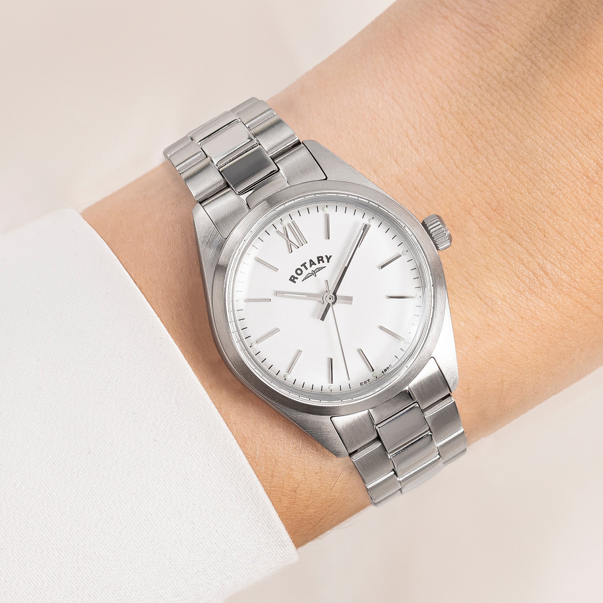 Silver Rotary wristwatch with white dial on a wrist against a light background