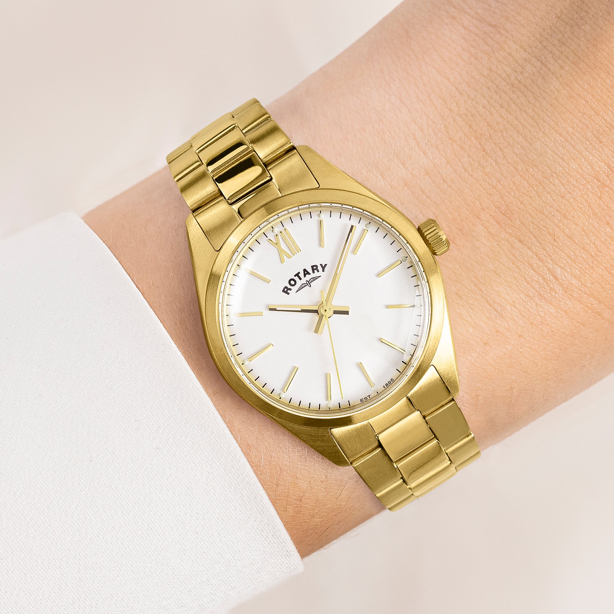 Gold Rotary wristwatch with white face on a wrist against a light background