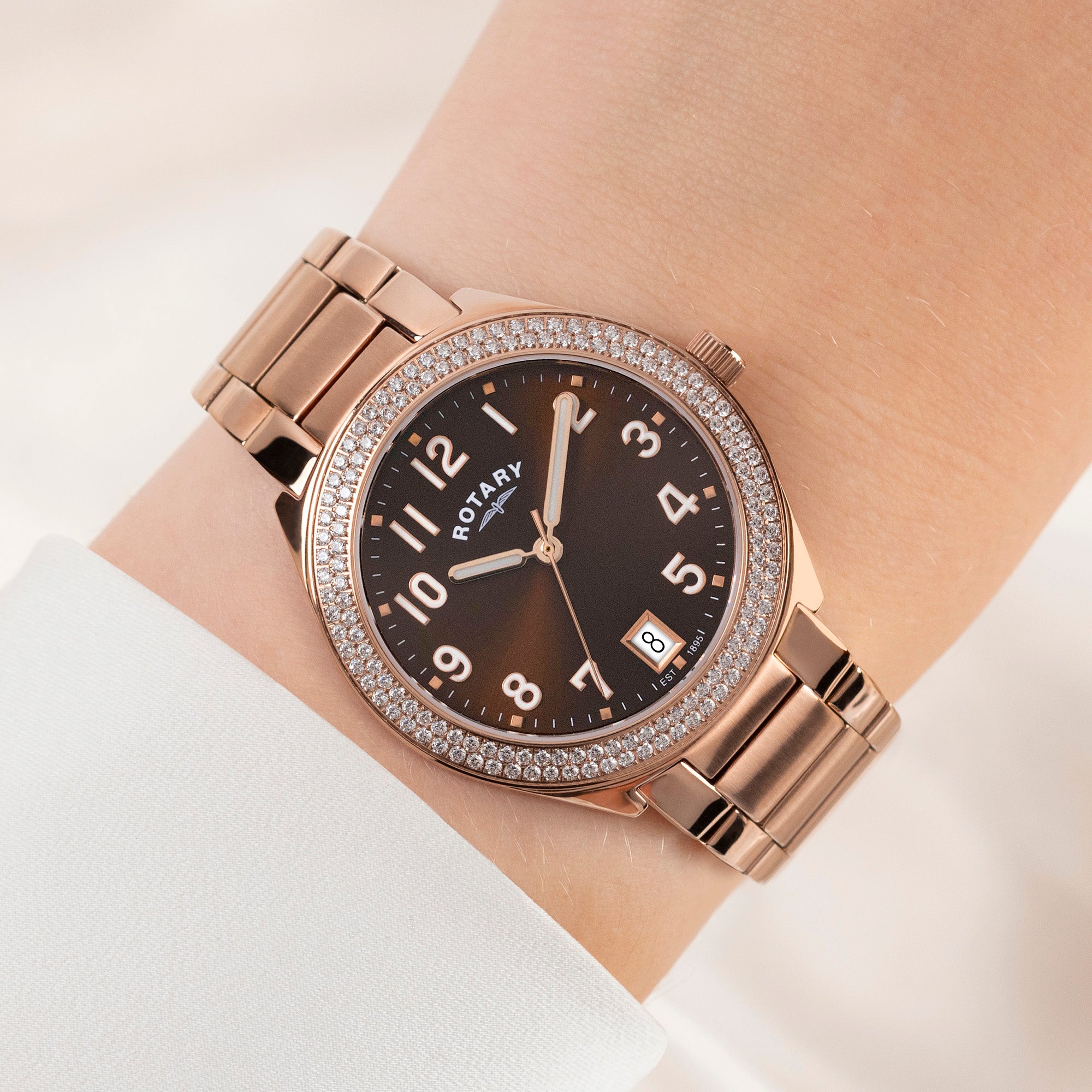 Rotary Brilliance rose gold watch with gem-set bezel on a wrist against a light background