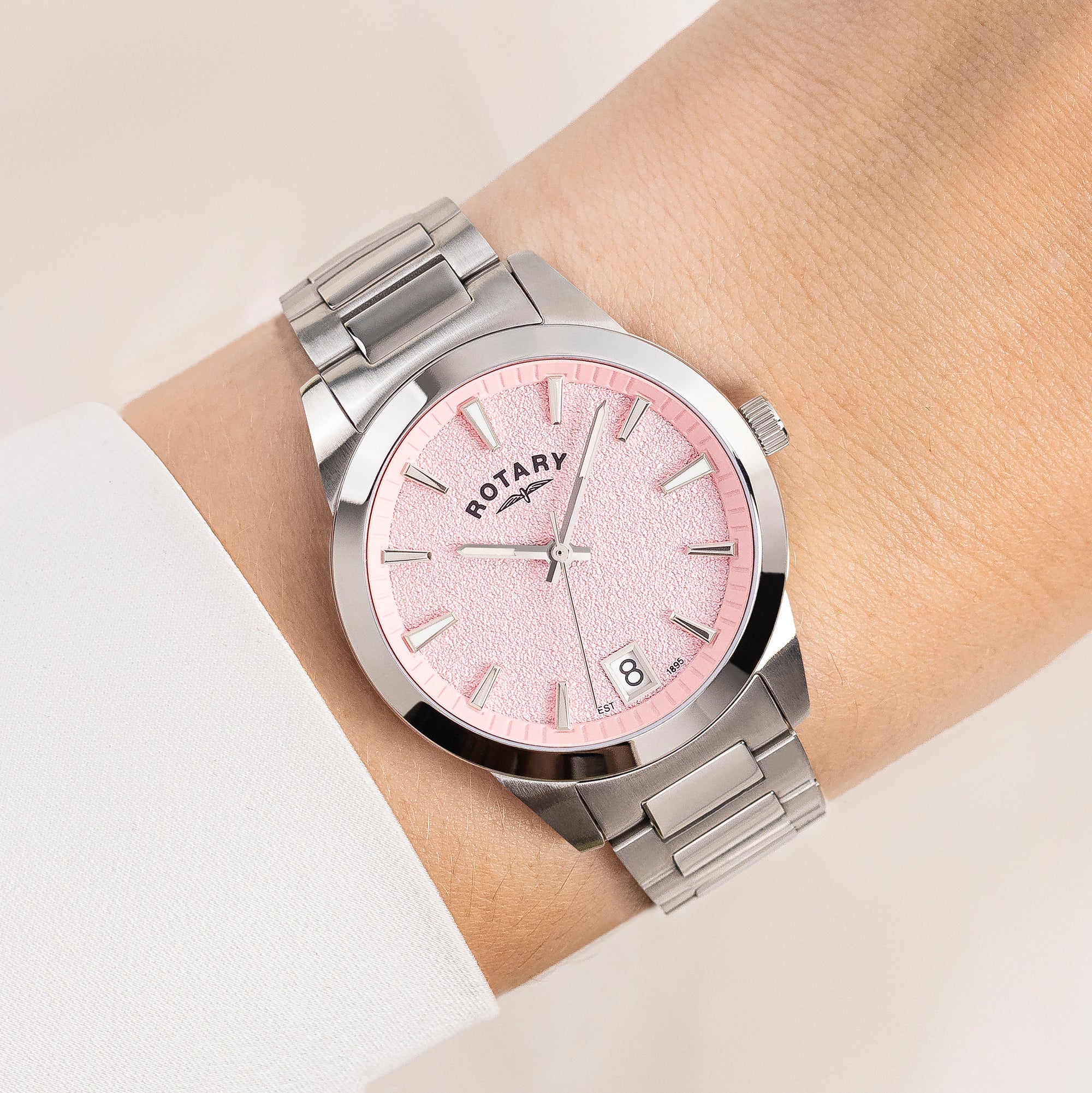 Silver Rotary watch with a pink face on a wrist against a neutral background