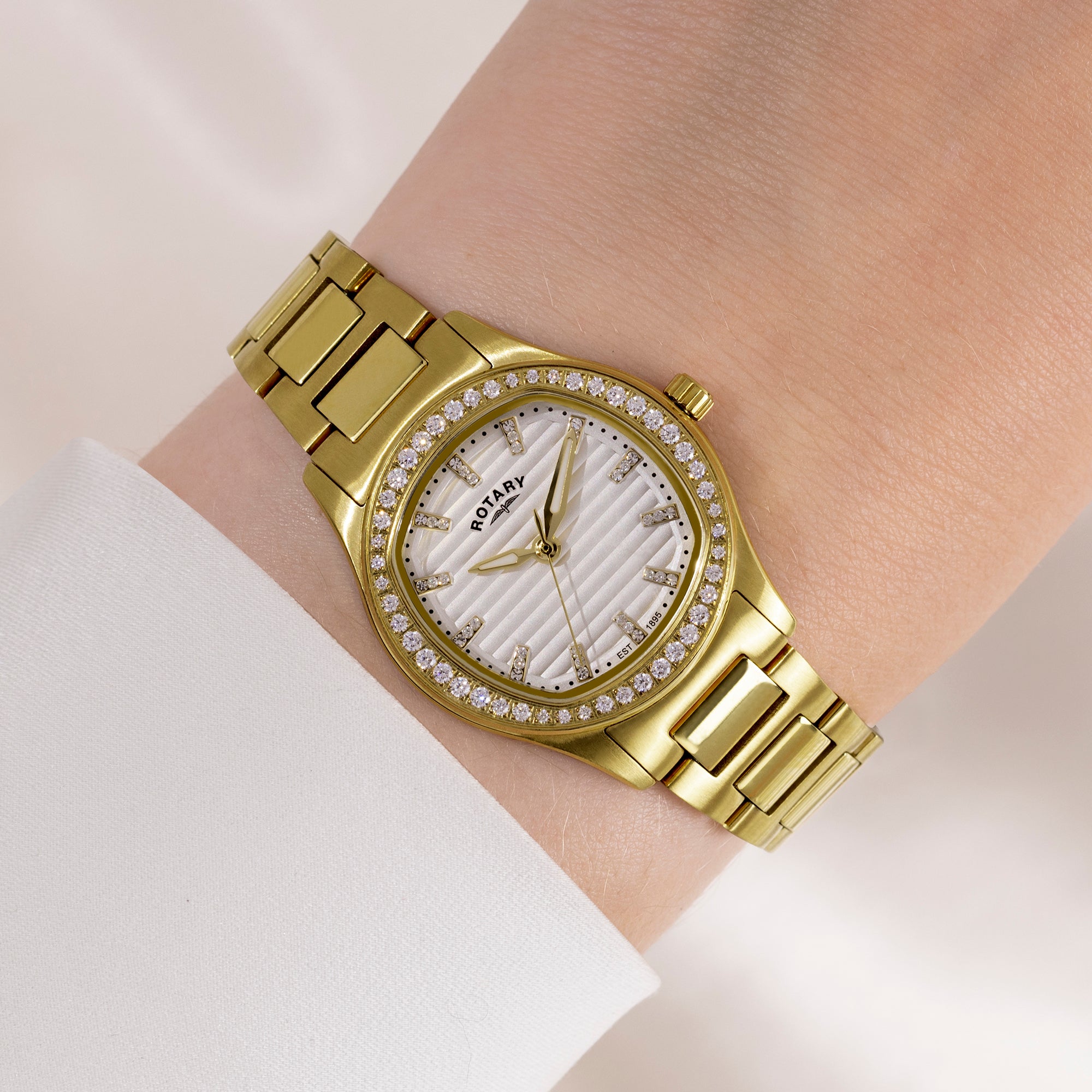 Gold rotary wristwatch with gemstone accents on a wrist against a light background