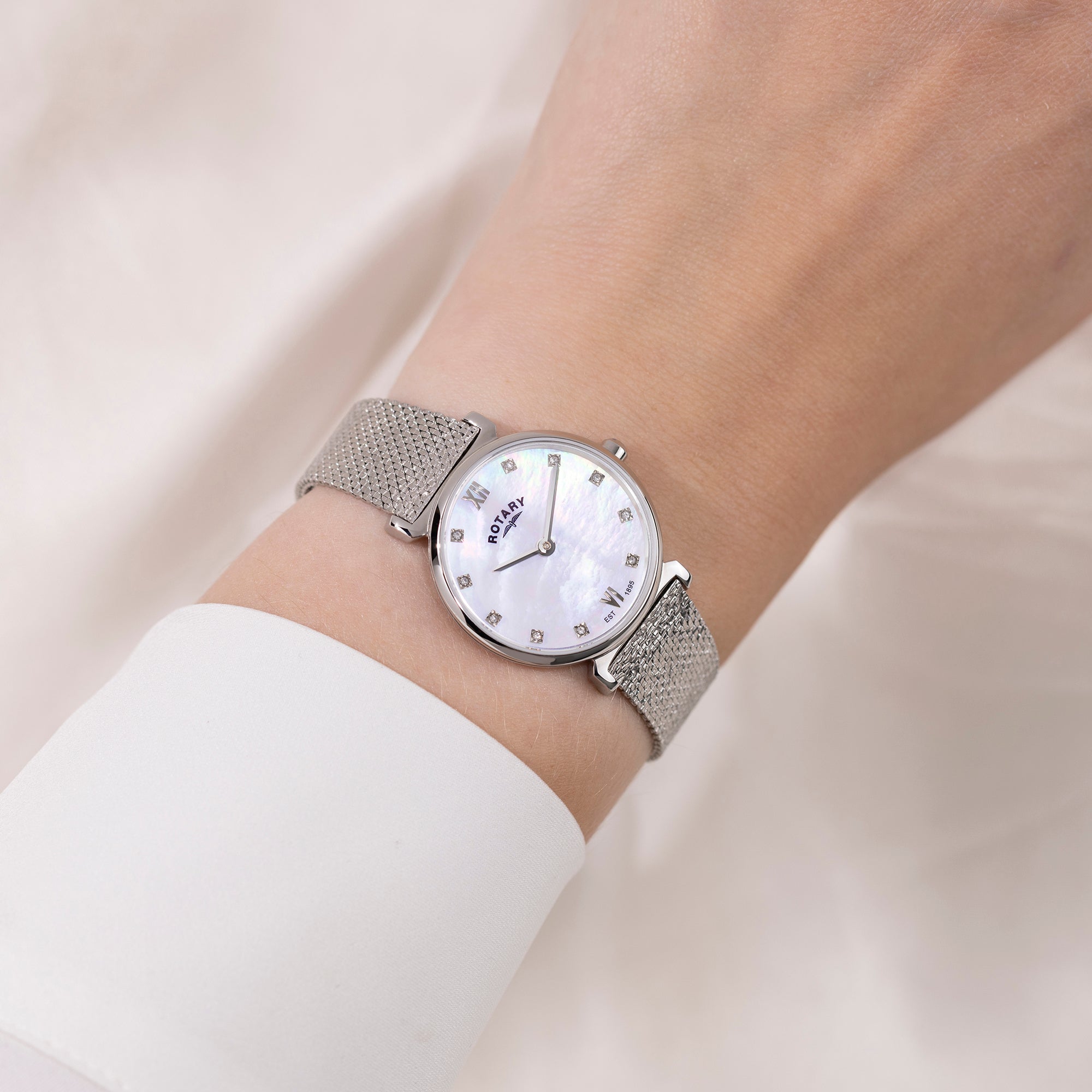 Silver Rotary watch with a mesh band on a wrist against a light background