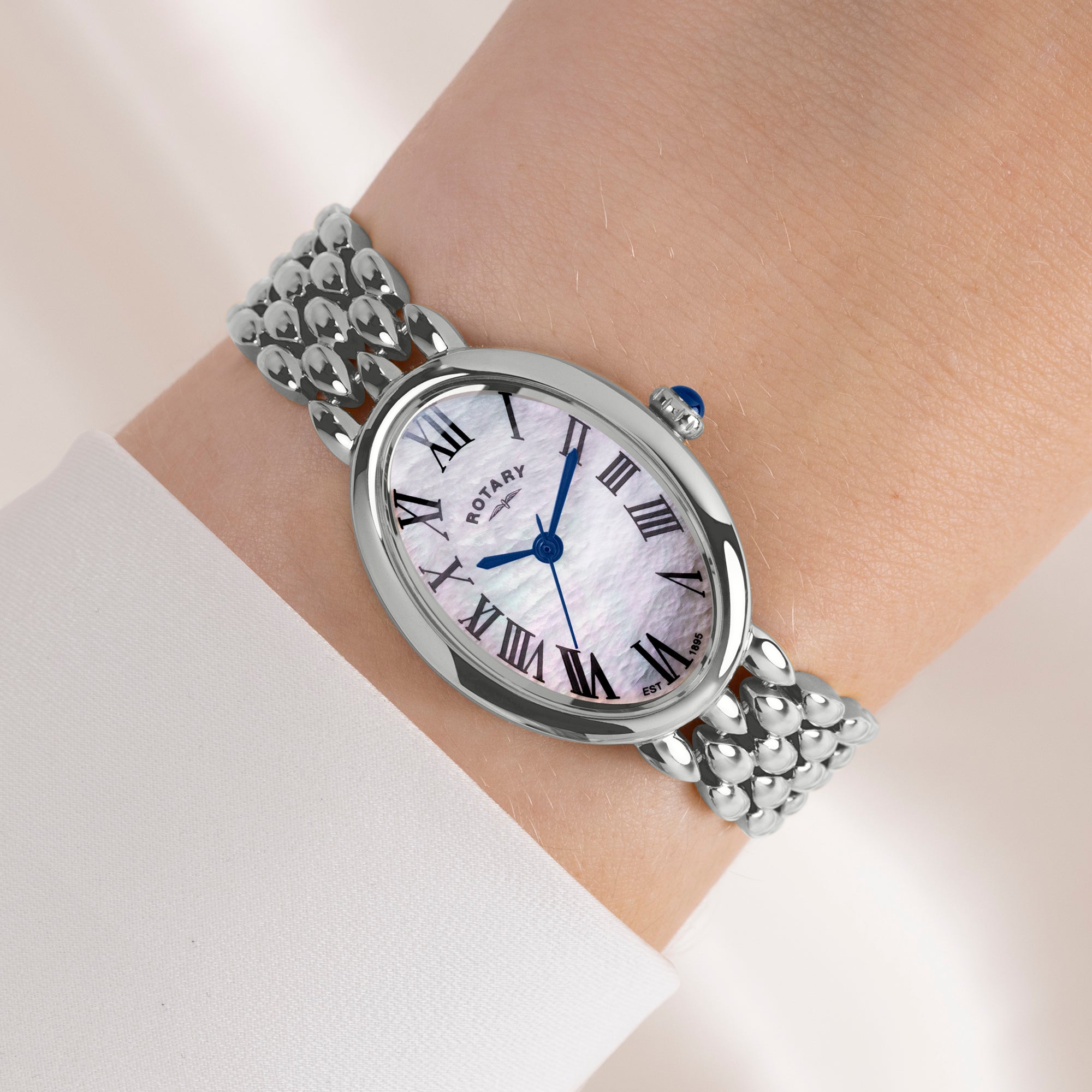 Silver Rotary watch with a mother of pearl dial and Roman numerals on a wrist against a light background