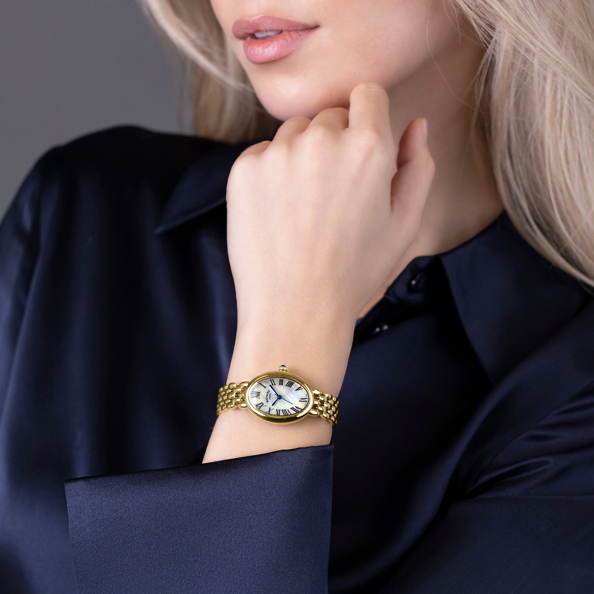 Woman wearing a gold Rotary Heritage Astoria watch on her wrist with a neutral background