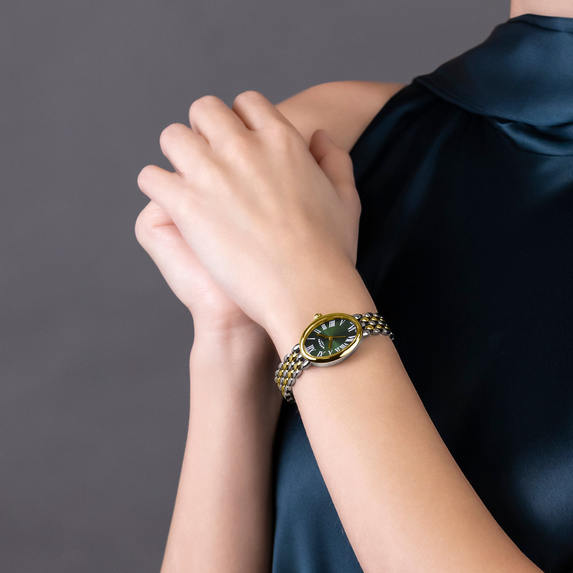 Person wearing a two-tone Rotary Heritage Astoria watch with a dark green face on a gray background