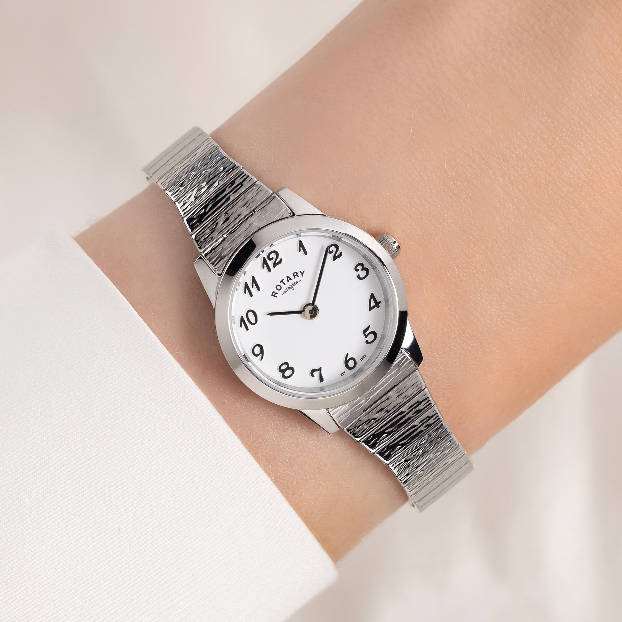 Silver Rotary watch with a white face on a wrist against a light background