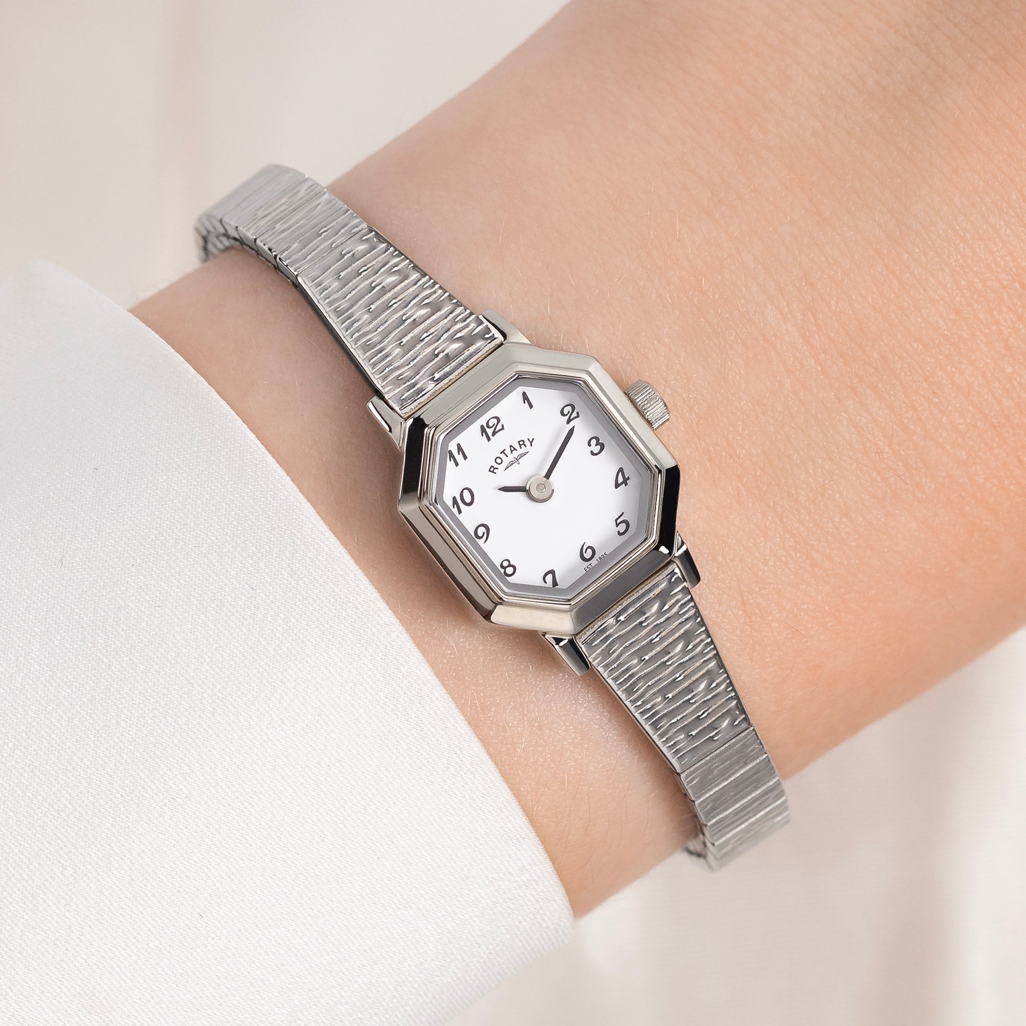 Silver Rotary watch with a white face on a wrist against a light background